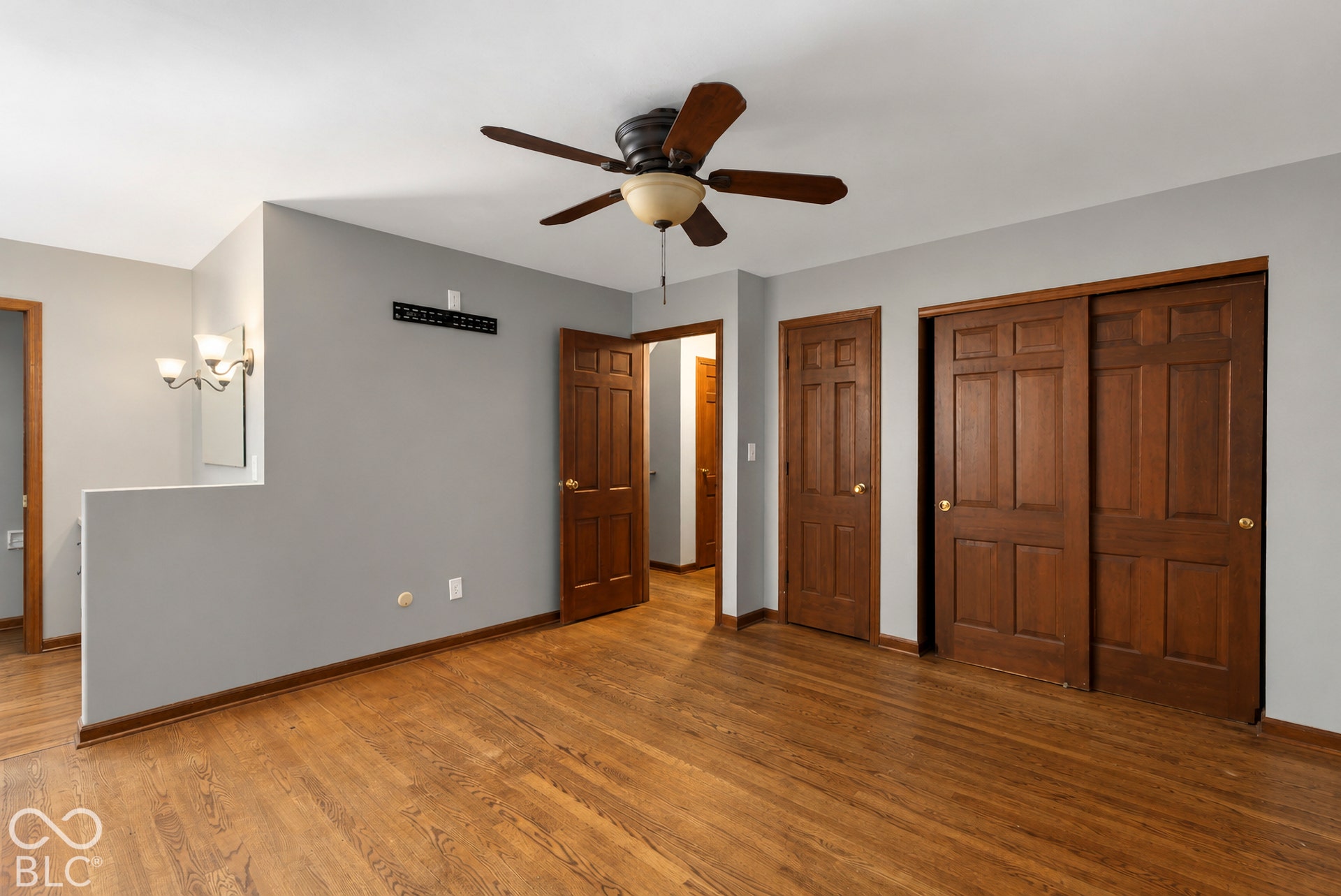 Wood-finish flooring, six-panel wood doors, sliding closet doors, multi-blade ceiling fan, and wall-mounted light fixture