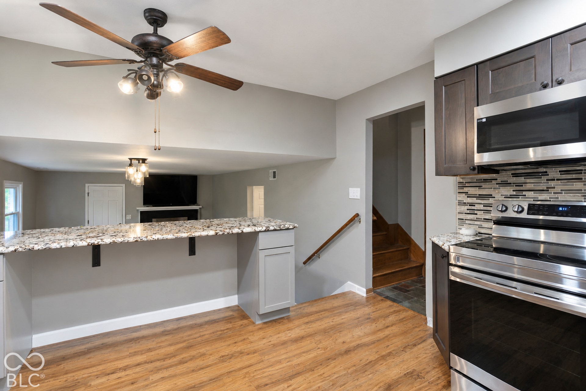 Kitchen featuring dark cabinetry, a stone-surfaced breakfast bar, stainless steel appliances, a multi-tone tile backsplash, and wood-finish flooring