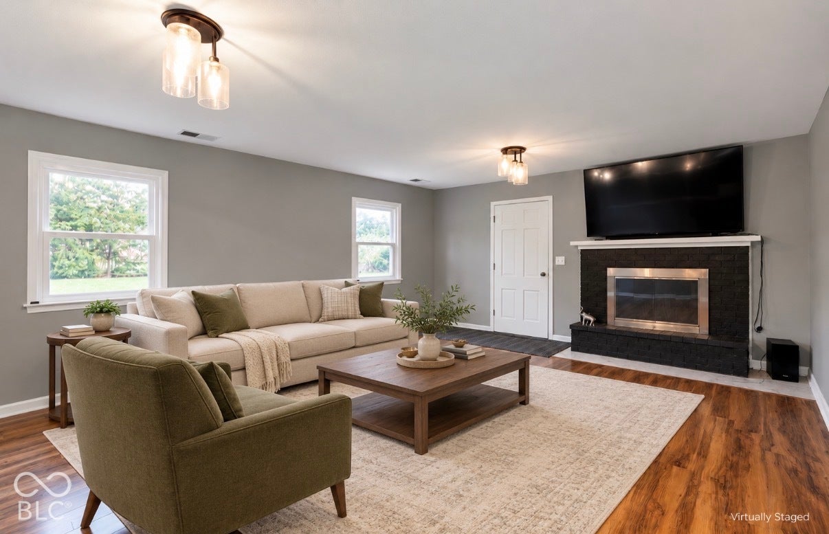 Virtually Altered - Living area featuring wood-finish flooring, dual-pane windows, dual flush-mount ceiling light fixtures, and a black stone-finish fireplace with a built-in mantel