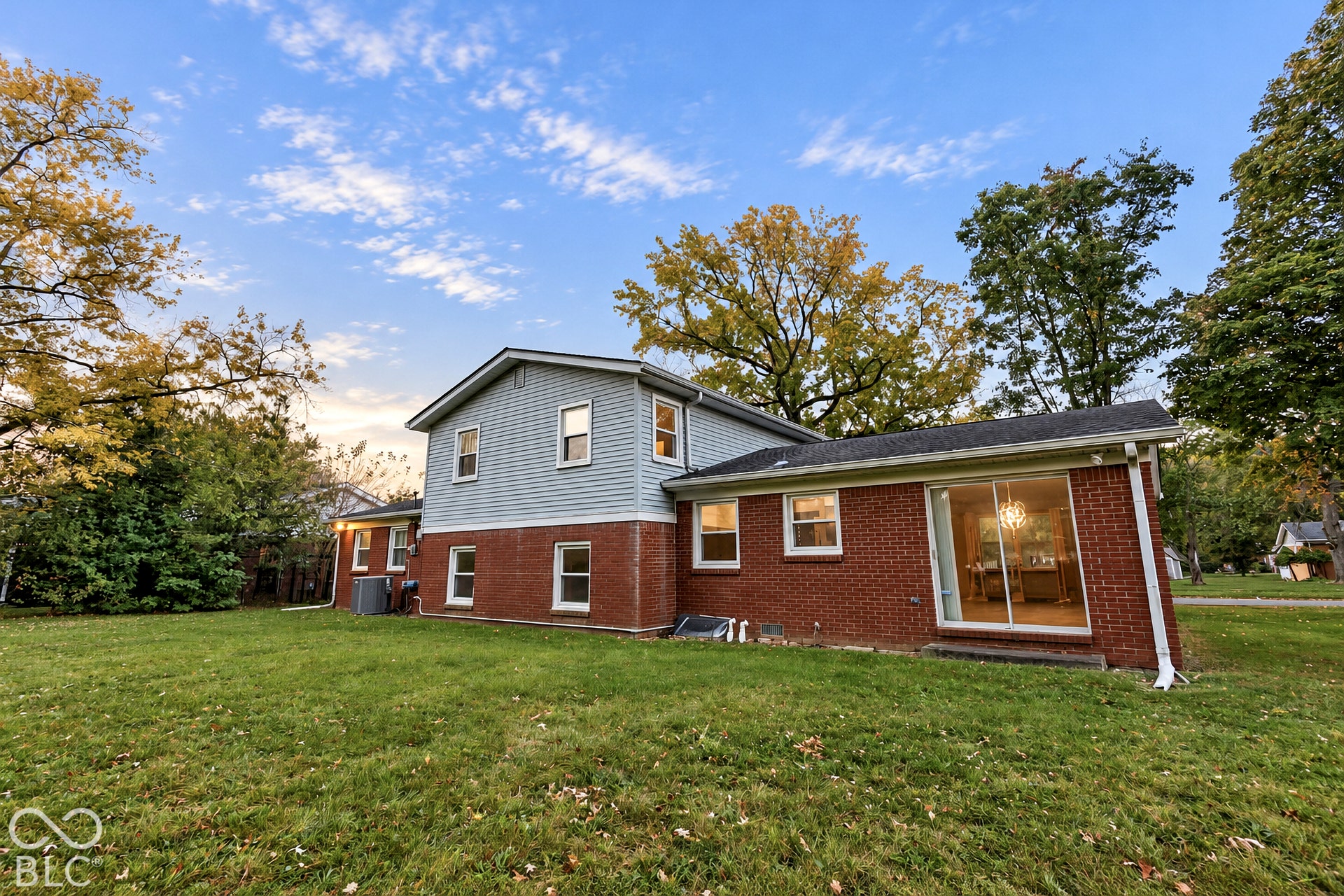 Two-story exterior featuring a brick and horizontal siding facade, sliding glass patio doors, and a spacious lawn with mature trees