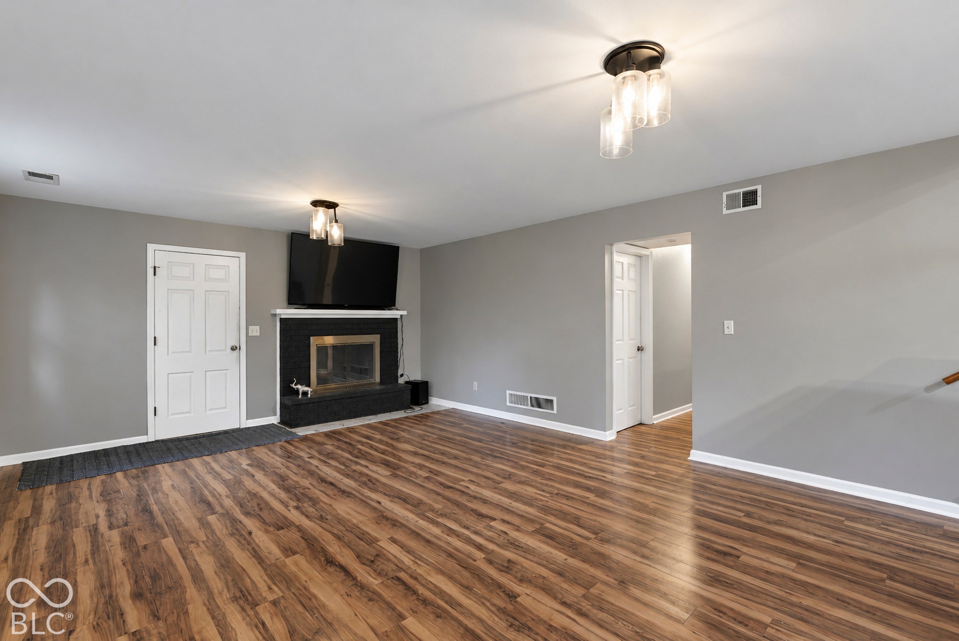 Living area featuring wood-finish flooring, a masonry fireplace with a tiled surround, and multi-light flush-mount fixtures