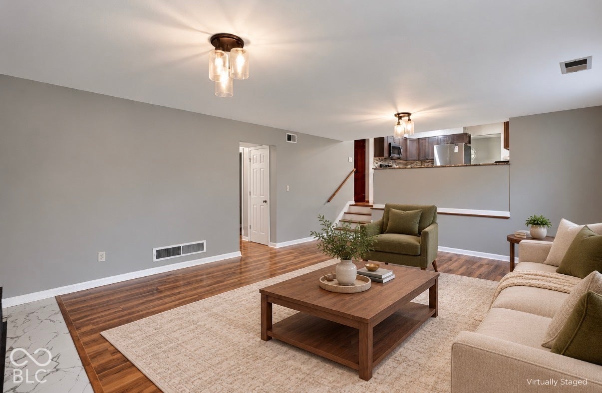 Virtually Altered - Living area featuring wood-finish flooring, two multi-light flush-mount fixtures, and stairs with wood railings