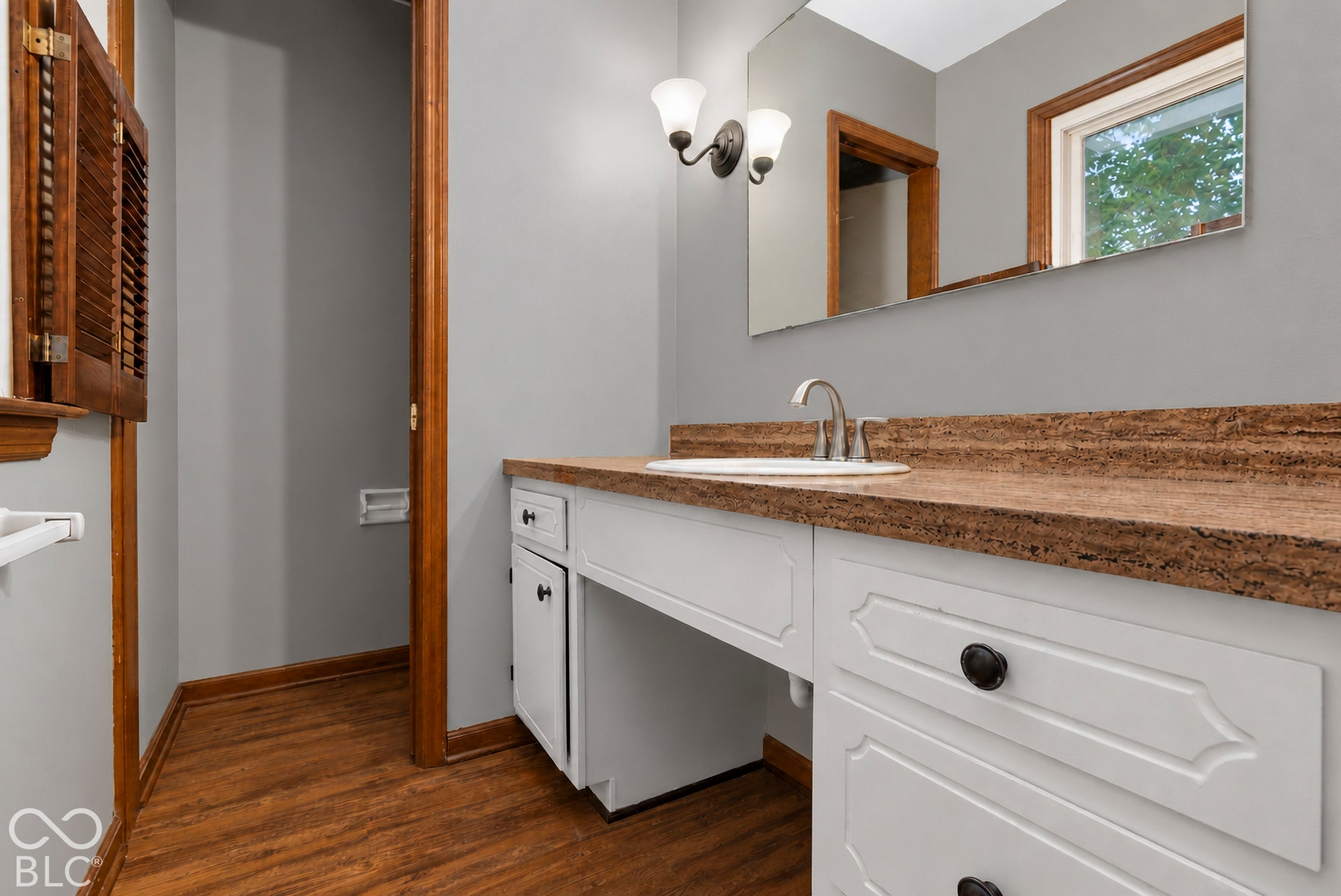 White cabinetry with recessed-panel doors, solid surface countertop, undermount sink, wood-finish flooring, and dual-light vanity fixture