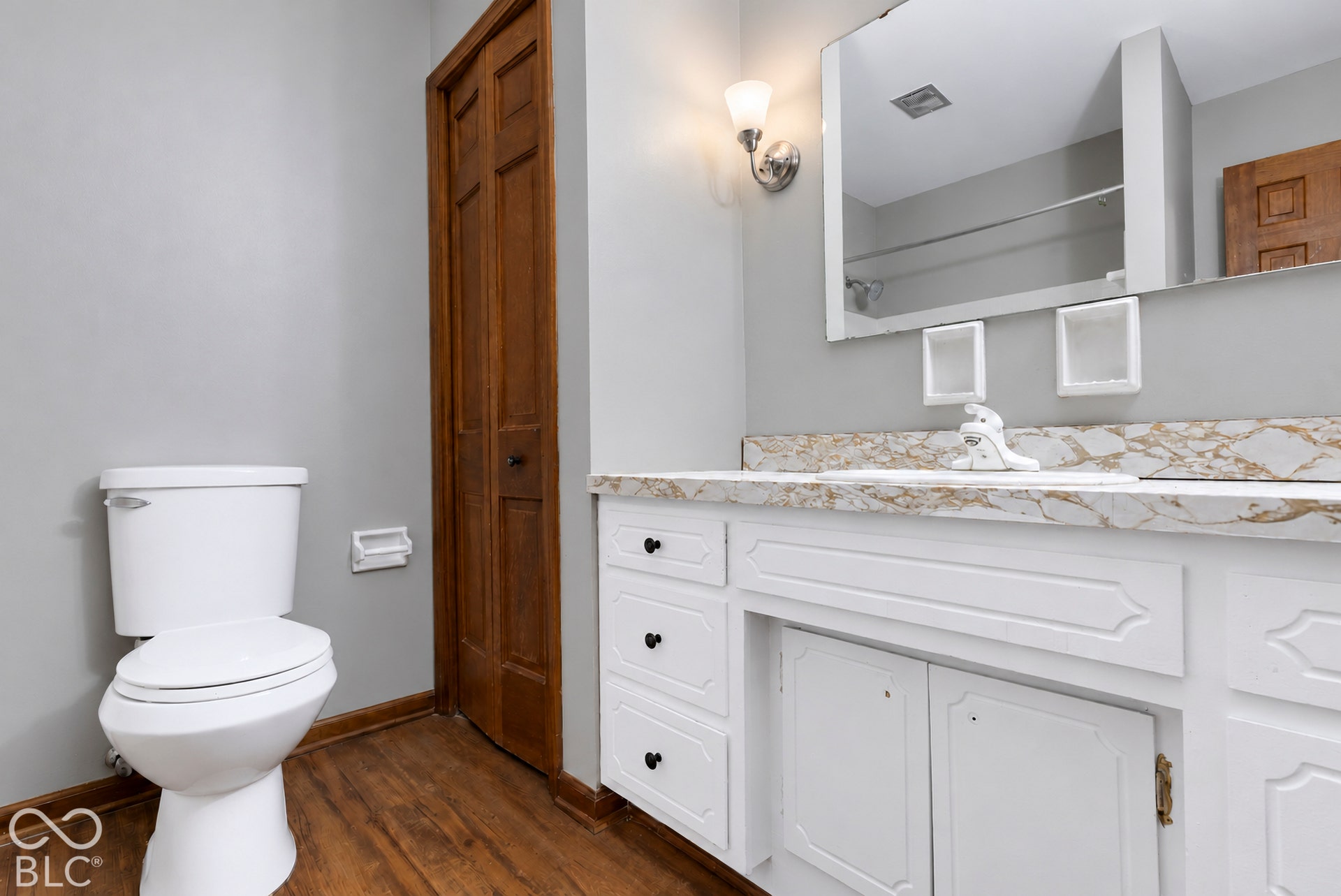 Bathroom featuring white cabinetry, stone-patterned vanity countertop, wood-finish flooring, wall-mounted light fixture, and framed wall mirror
