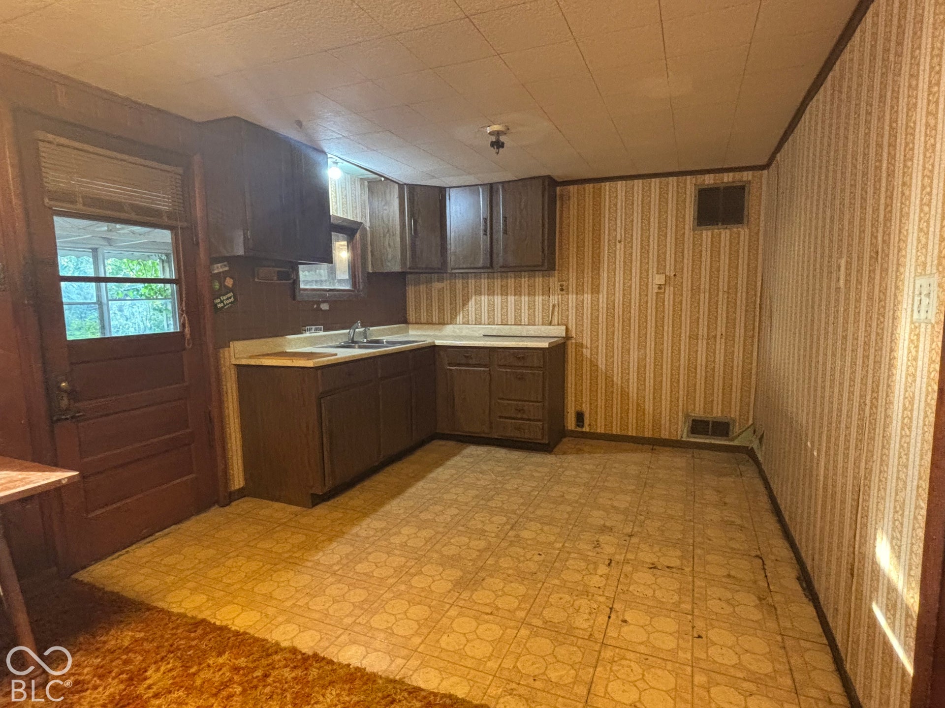Kitchen featuring dark wood-finish cabinetry, solid-surface countertops, a stainless steel dual-basin sink, and patterned vinyl flooring