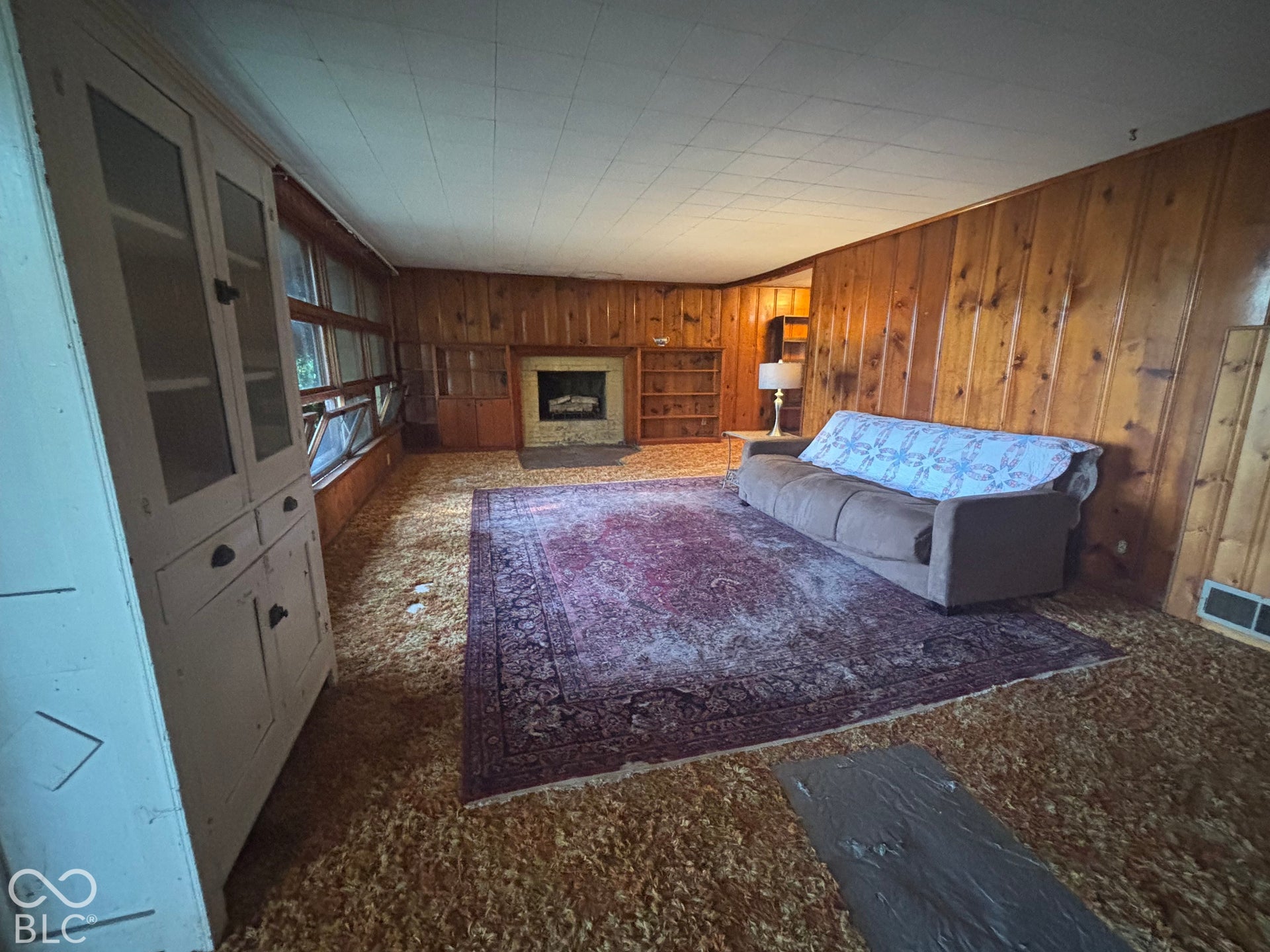 Wood-paneled interior featuring a masonry fireplace, built-in shelving, and a white, full-height glass-paneled storage cabinet