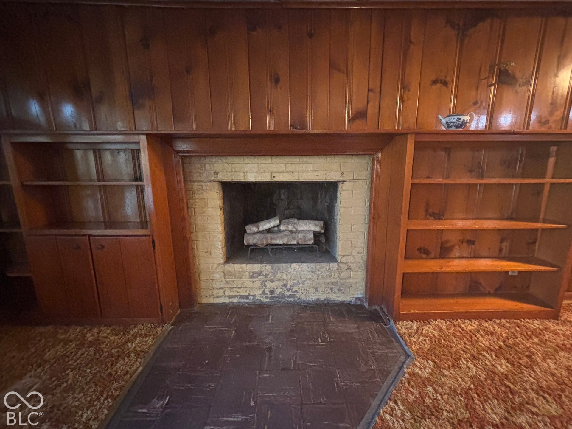 Fireplace featuring a painted brick surround, dark masonry hearth, and built-in wood-finish cabinetry with integrated shelving