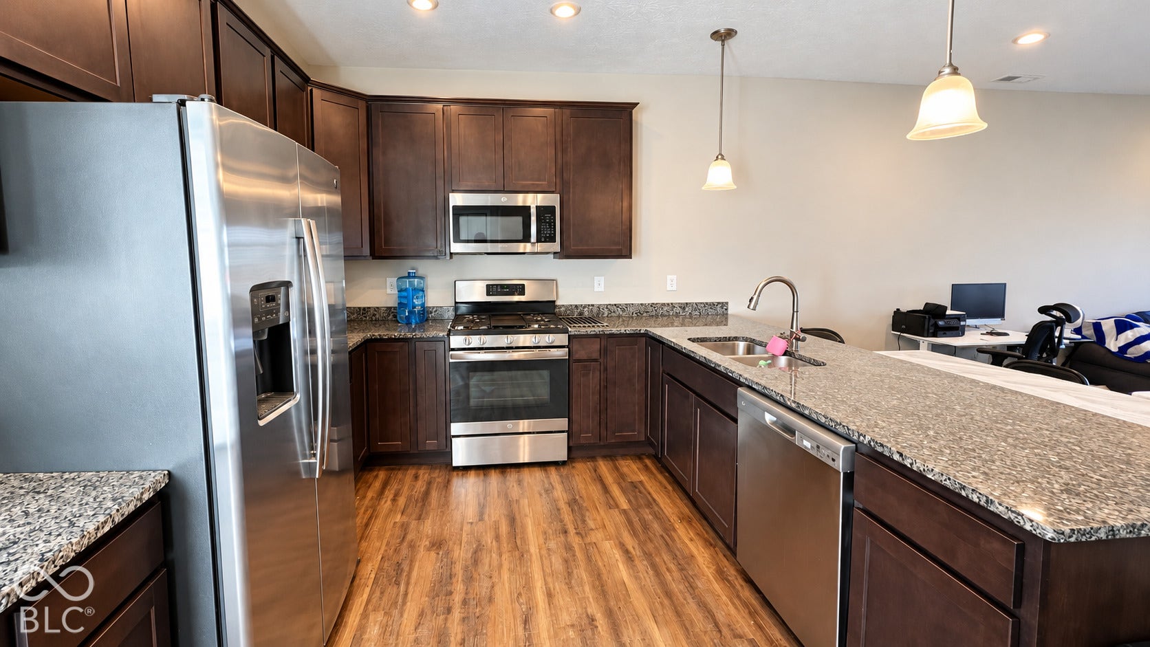 Kitchen featuring dark-finish wood cabinetry, stone-style countertops, stainless steel appliances, wood-finish flooring, and dual pendant lighting