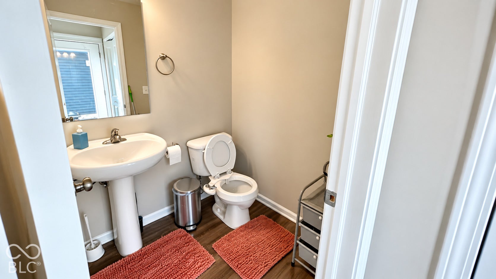 Powder room featuring a pedestal sink, dual-handle faucet, wall-mounted vanity mirror, and wood-finish flooring
