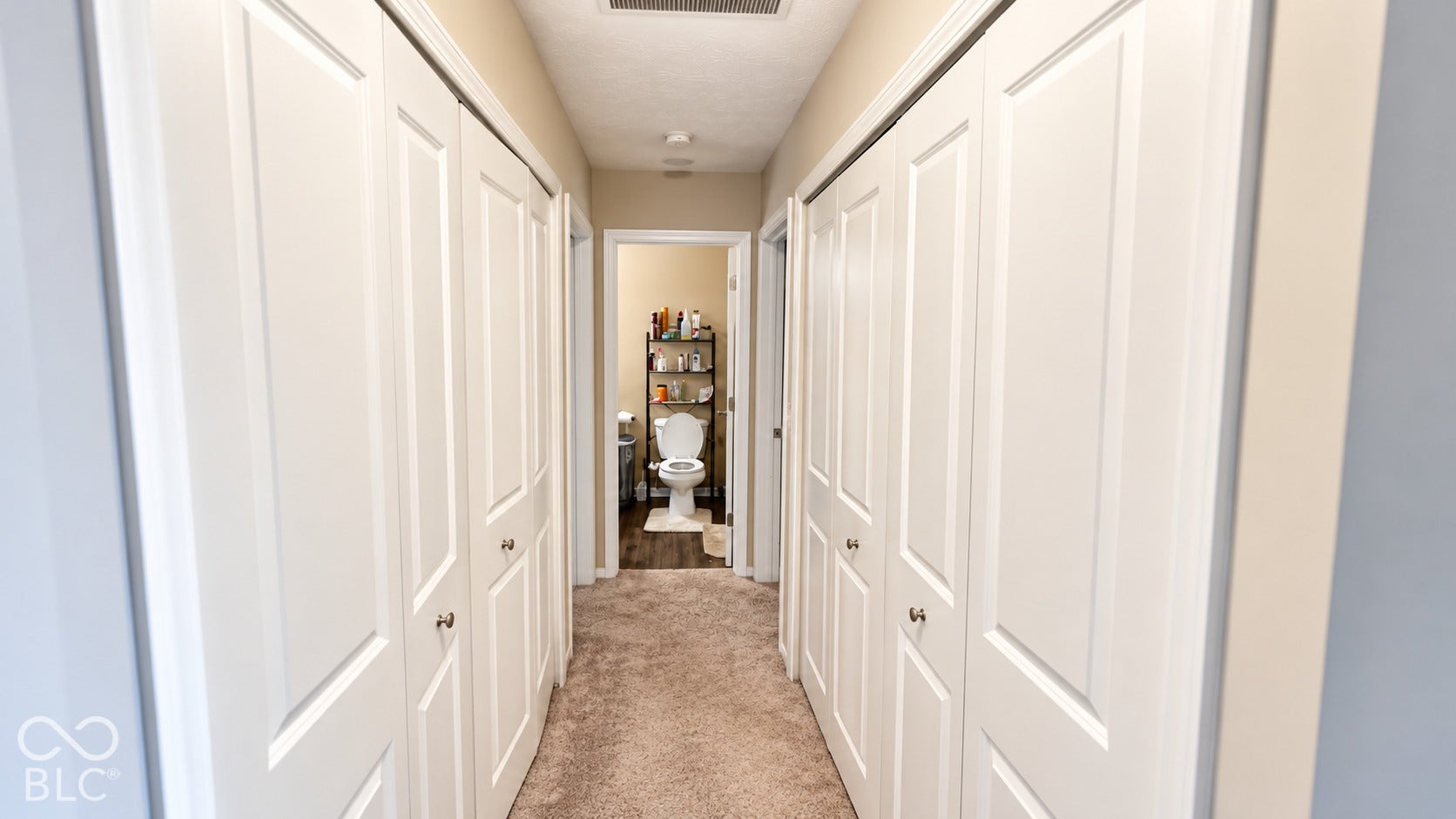 Hallway featuring four white multi-panel bi-fold doors and neutral carpeting