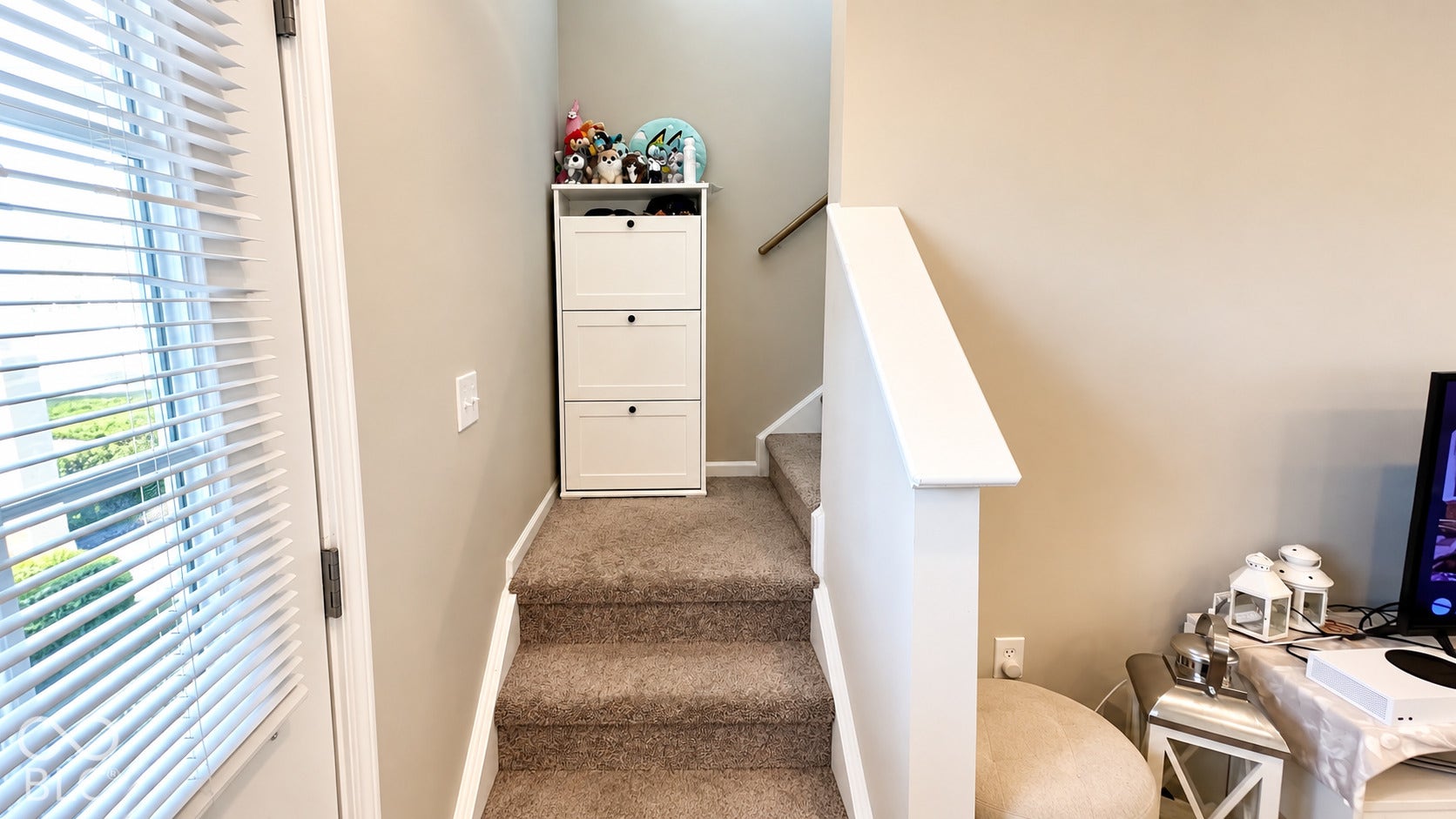 Staircase featuring neutral-toned carpeting, a white painted pony wall, and a wooden handrail