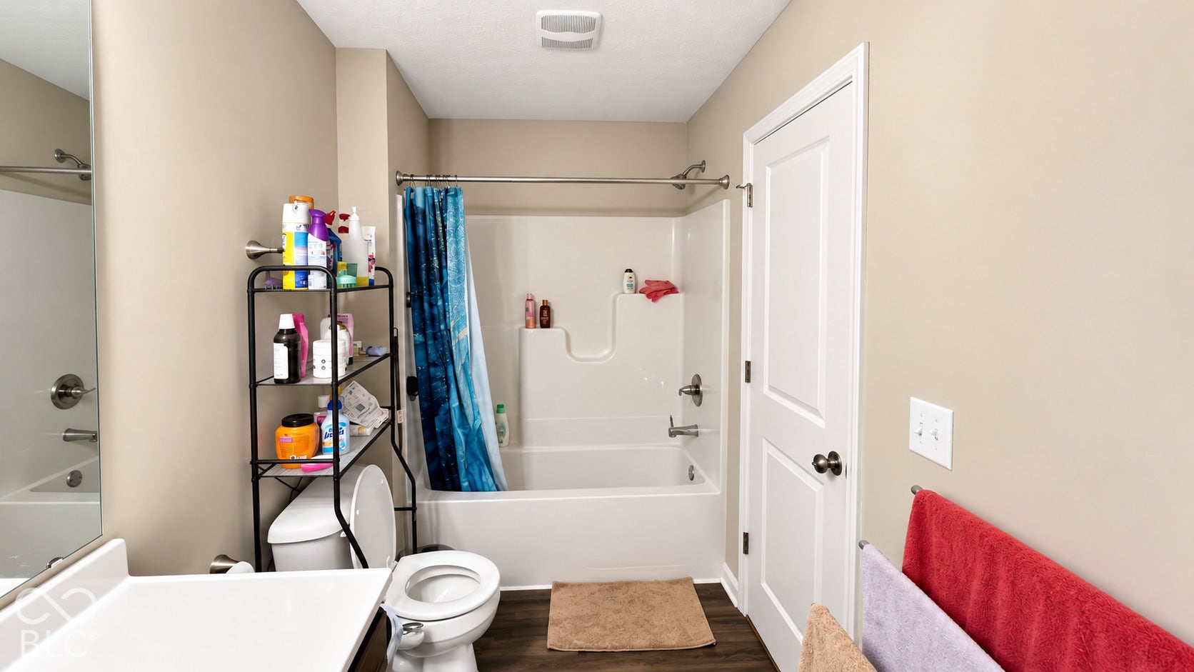 Bathroom featuring a tub and shower combination with a molded surround, large vanity mirror, wood-finish flooring, and a two-panel interior door