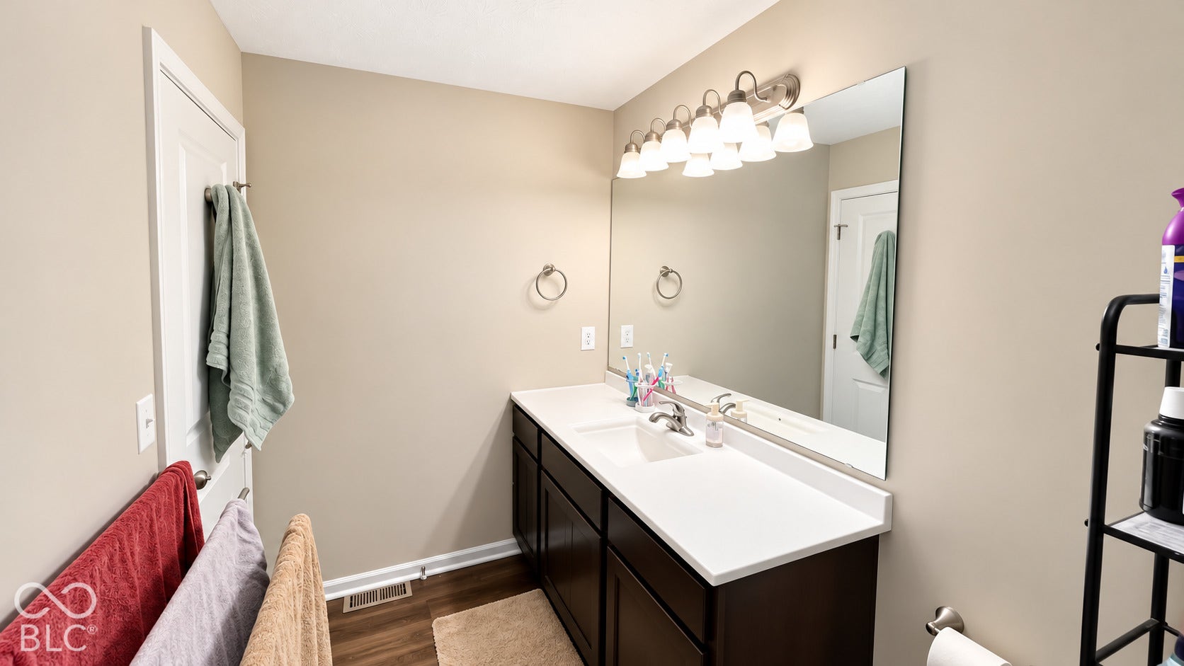 Bathroom vanity featuring a dark-finish wood cabinet, solid-surface countertop with an integrated rectangular sink, wall-spanning mirror, and multi-bulb light fixture