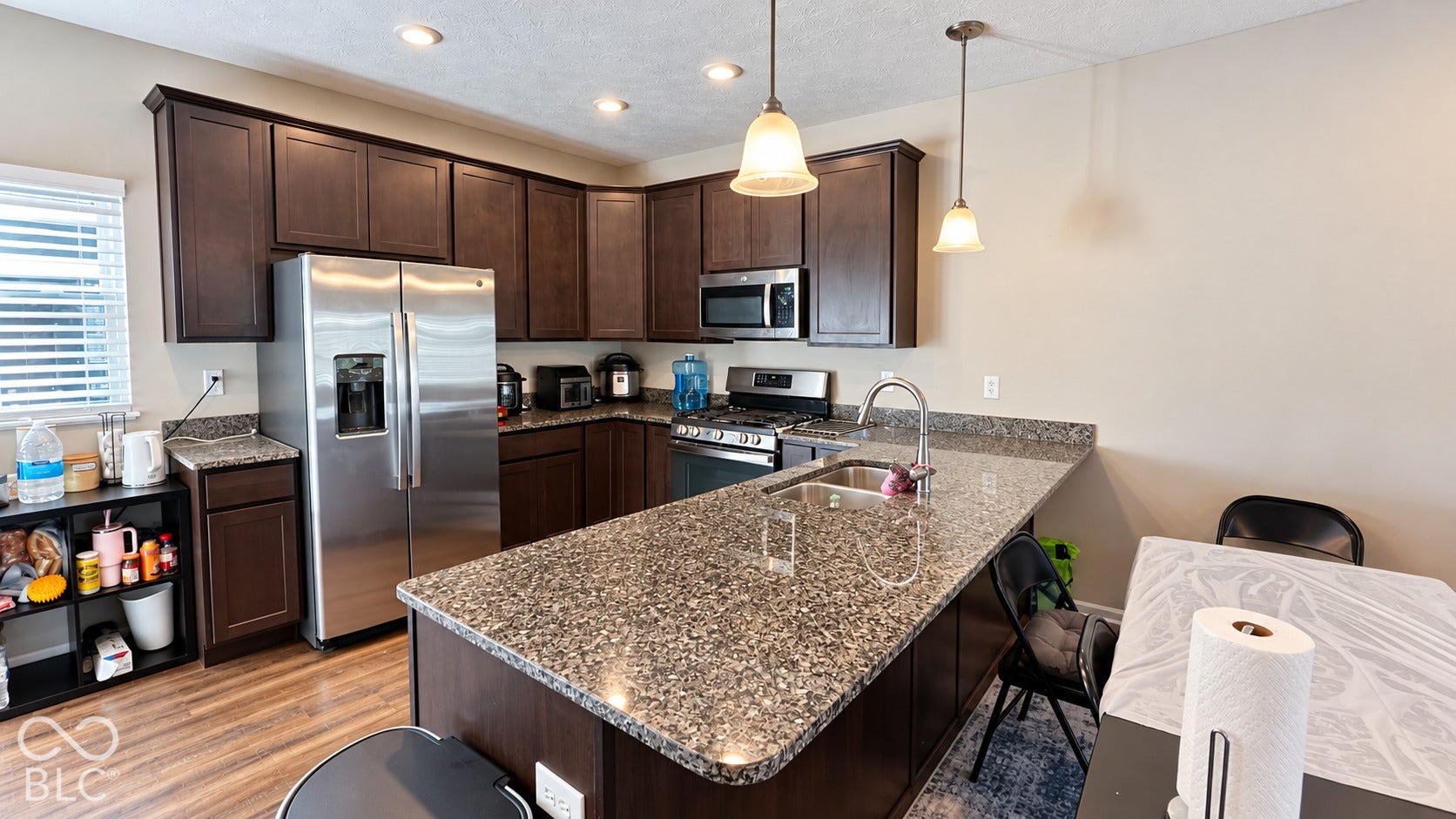 Kitchen featuring dark wood cabinetry, stone countertops, a stainless steel refrigerator, a built-in microwave, and pendant lighting