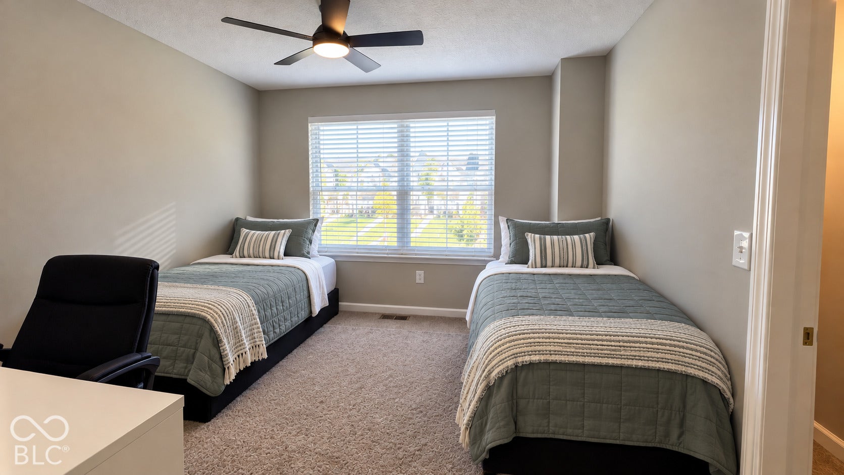 Neutral-toned bedroom featuring plush wall-to-wall carpeting, a multi-pane window with horizontal blinds, and a contemporary ceiling fan with integrated lighting