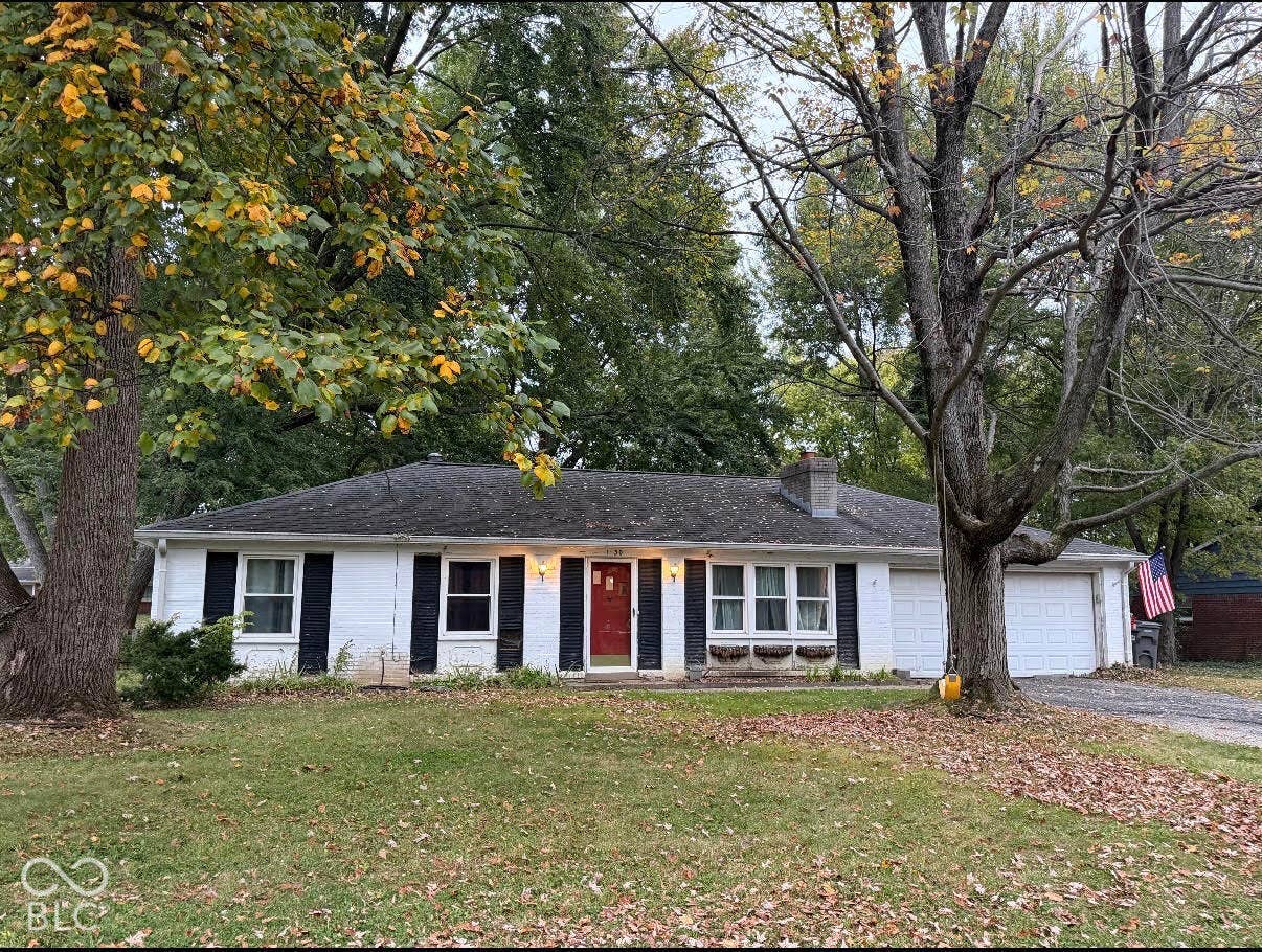 1630 W 76th Place, Indianapolis, IN 46260 Ranch-style exterior featuring painted brick masonry, dark-toned shutters, a centered front entry, and an attached two-car garage