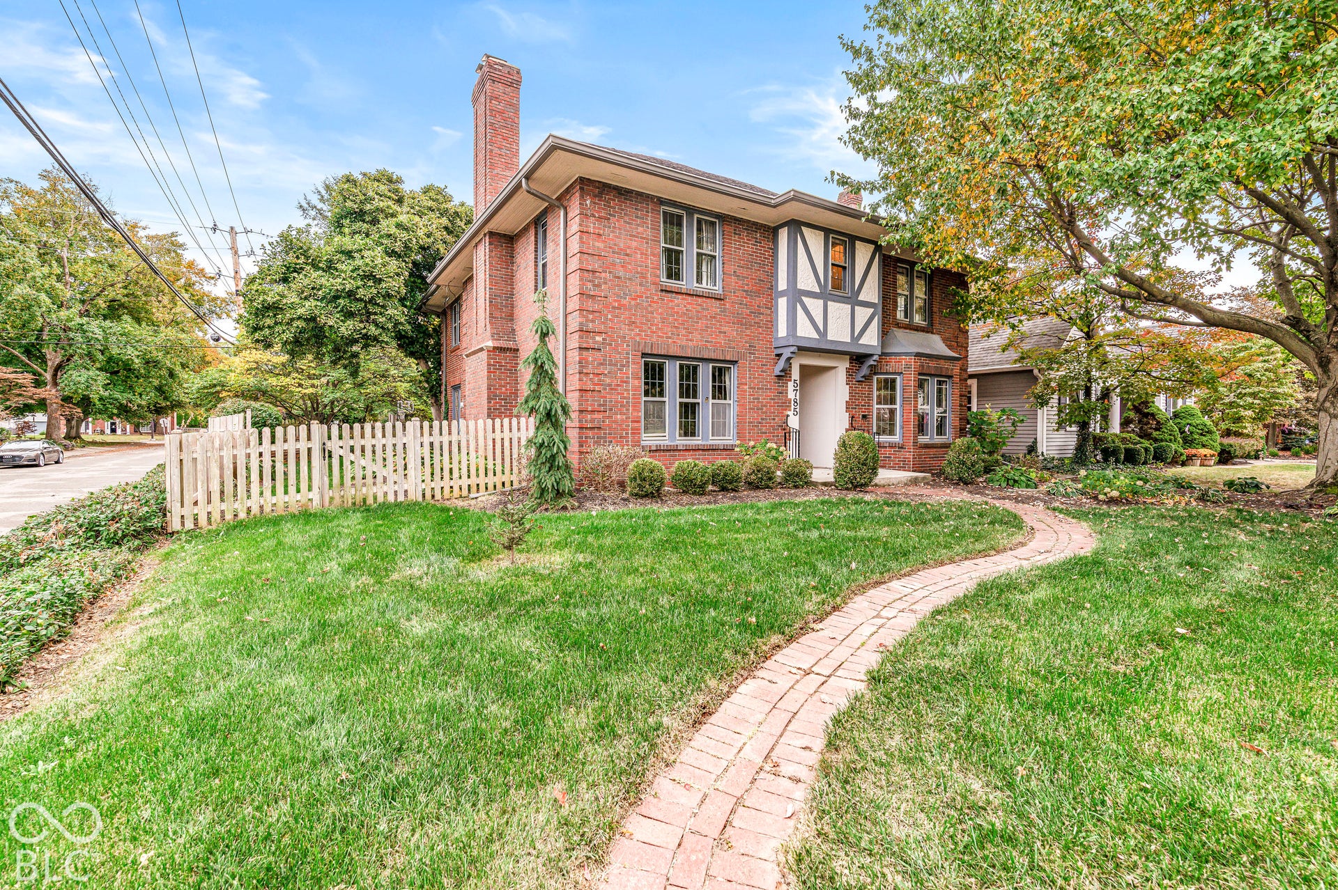 Traditional brick exterior featuring Tudor-style timber framing, a prominent chimney, multi-pane windows, and a paved brick pathway