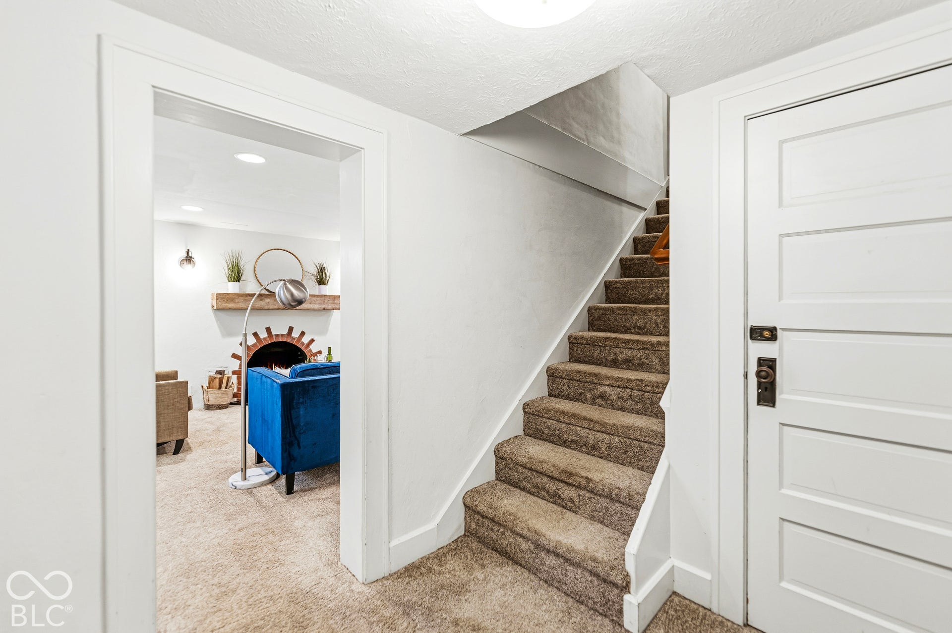 Carpeted staircase with white trim, five-panel interior door, and arched brick fireplace surround with a wooden mantel