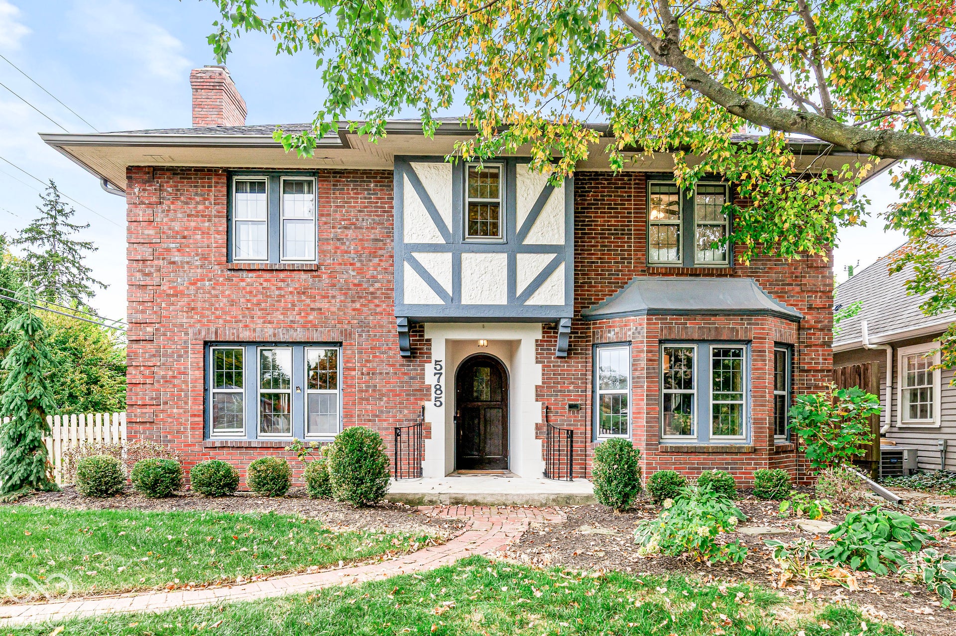 Tudor-style exterior featuring red brick masonry, decorative timber framing, a prominent bay window, and an arched entry door