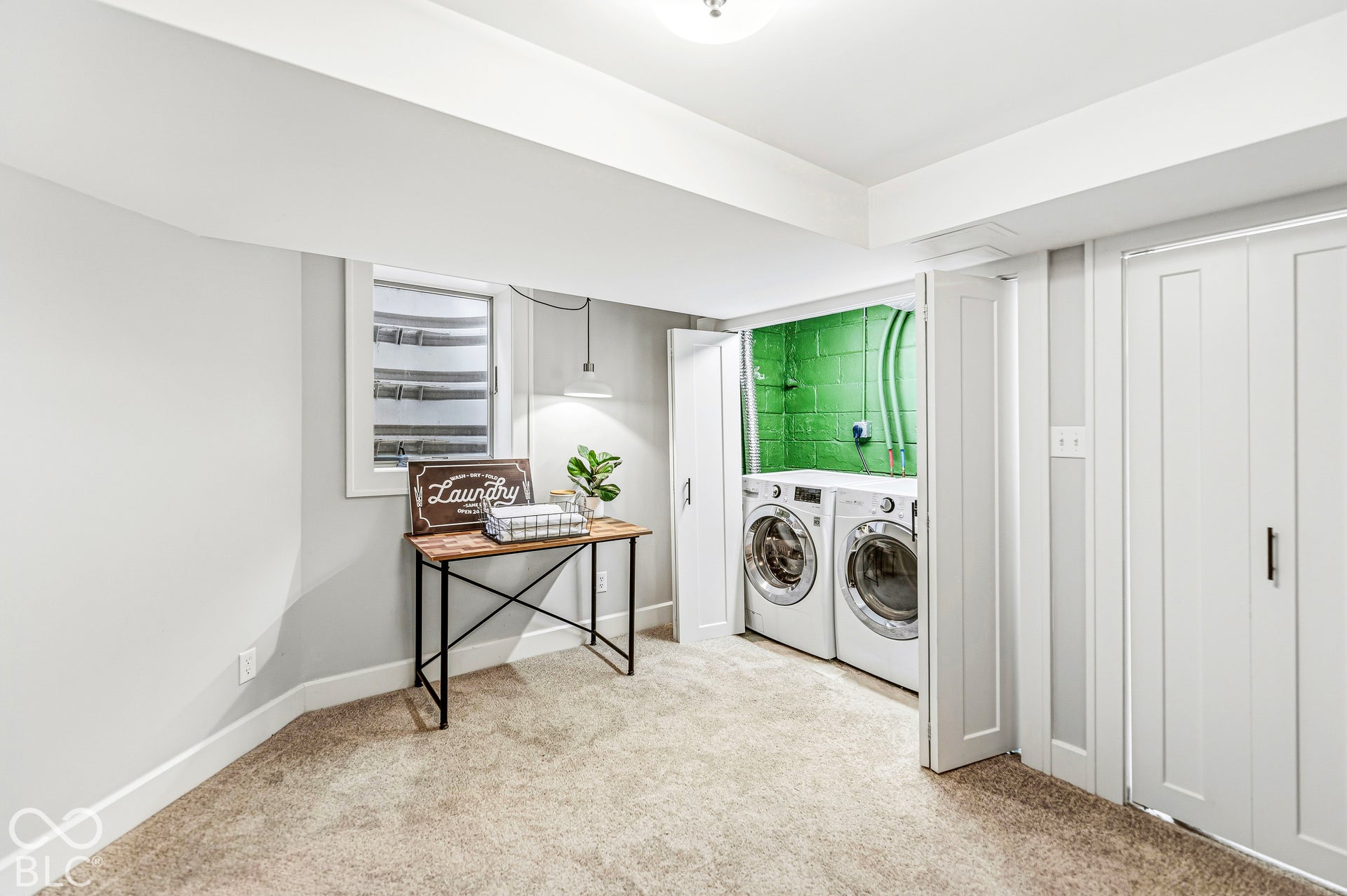 Utility area featuring a recessed laundry closet with dual bifold doors, wall-to-wall carpeting, and an egress window