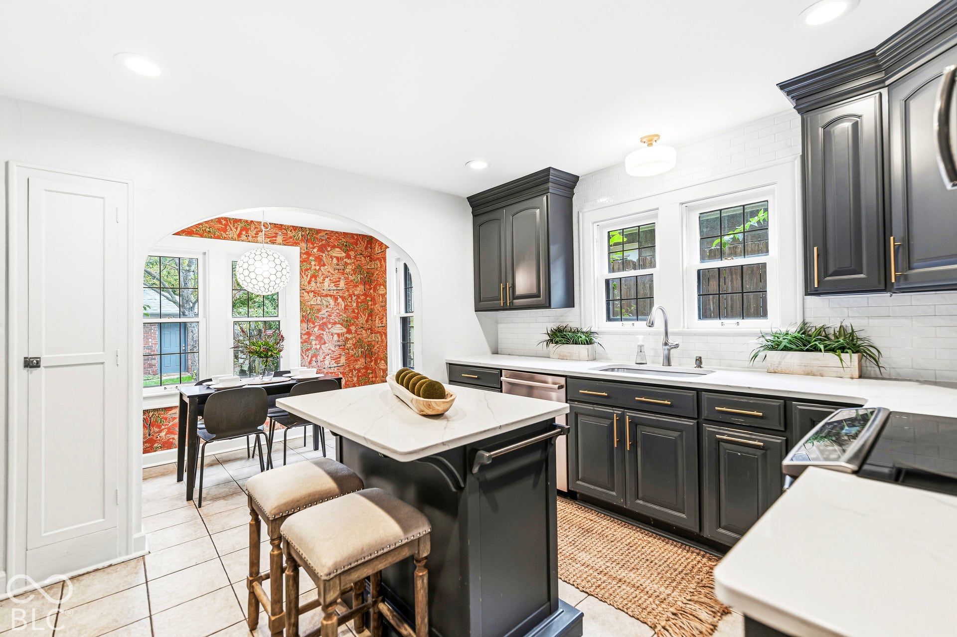 Kitchen featuring dark cabinetry with metallic hardware, stone countertops, central island, tiled flooring, and arched entryway