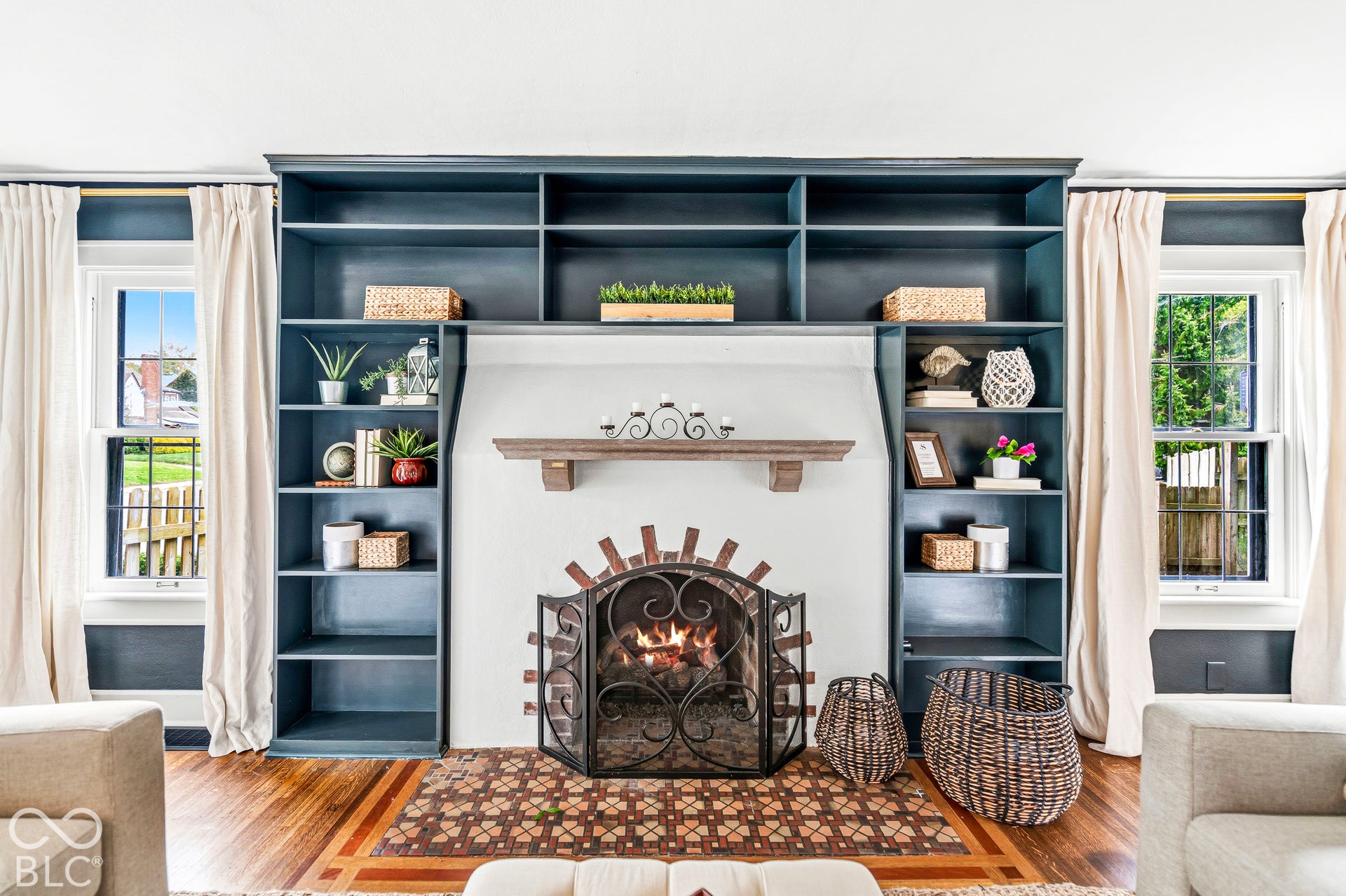 Floor-to-ceiling dark-toned built-in shelving, central fireplace with arched brick detailing, wood-finish flooring with decorative inlay, and wood mantel