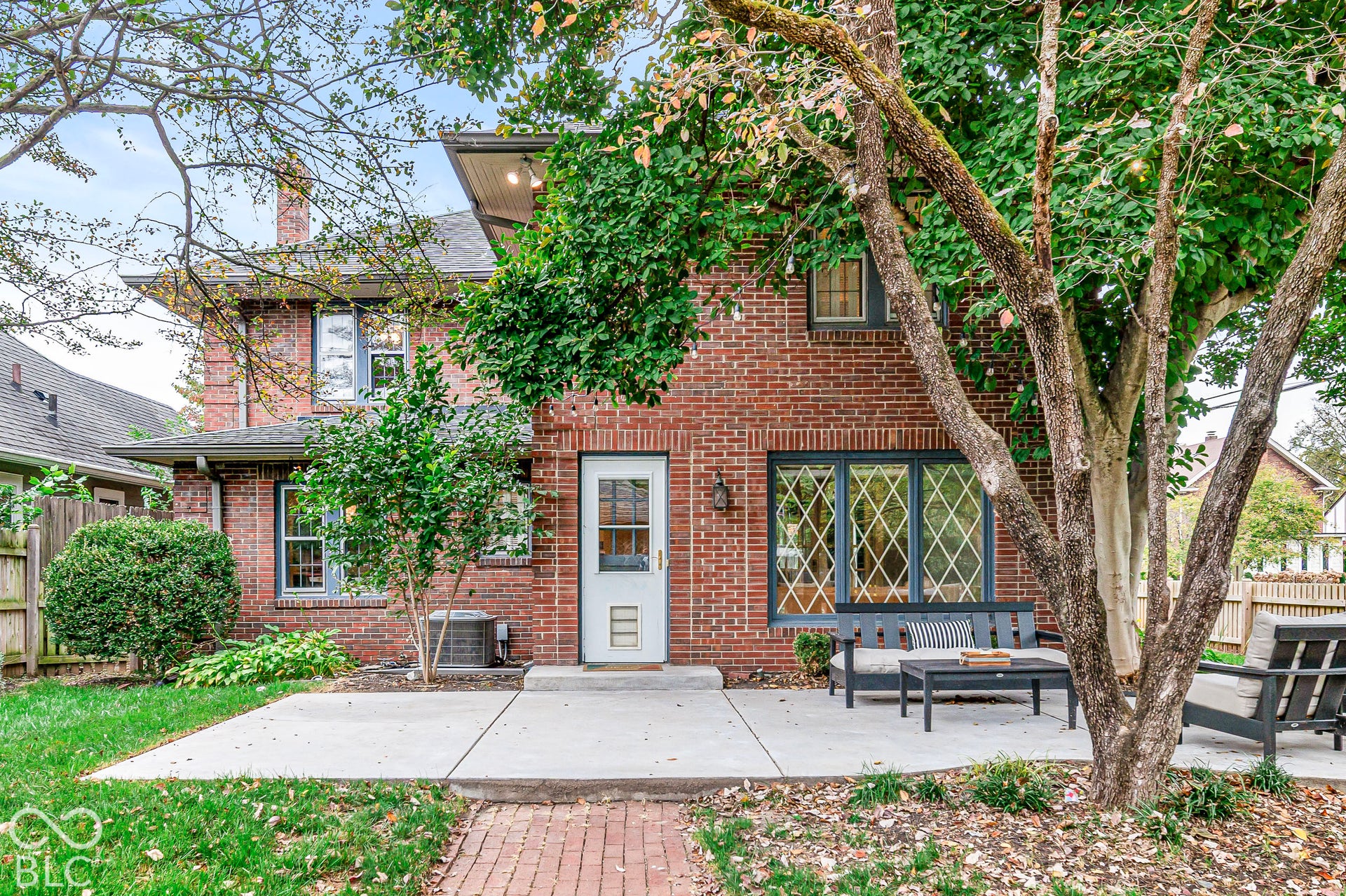 Brick exterior with concrete patio, lattice-style window detailing, and mature landscaping