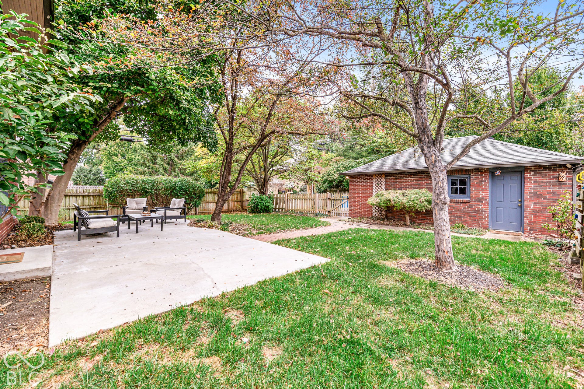 Private backyard featuring a concrete patio, brick detached garage, mature trees, and wood-fence perimeter