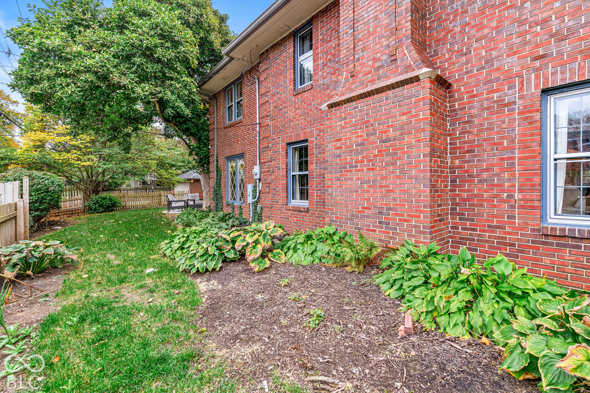 Red brick exterior featuring decorative leaded glass window detailing, mature landscape plantings, and a fenced yard