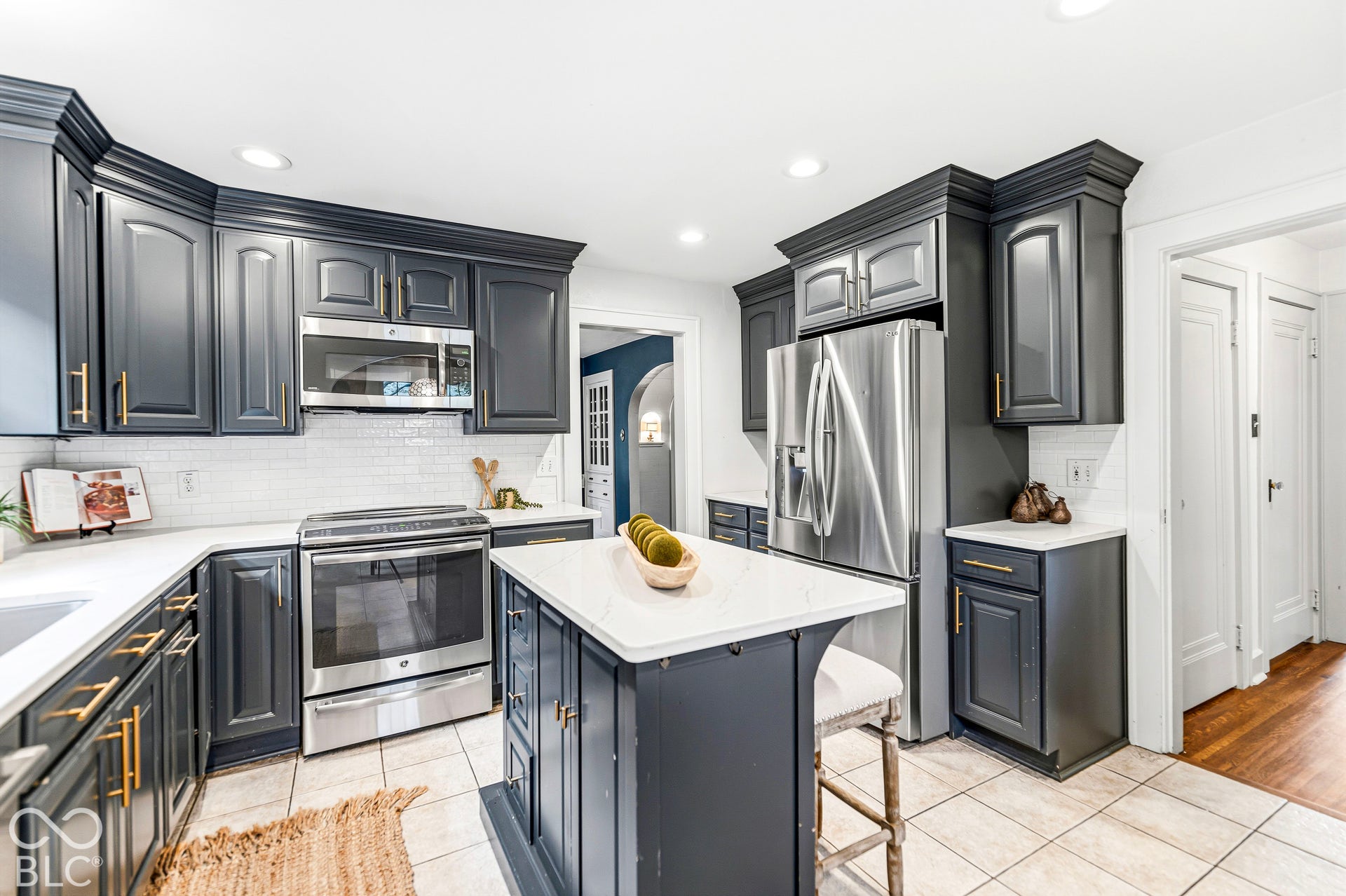 Dark cabinetry with brass-finish hardware, stainless steel appliances, stone-surface countertops, central island, and white tile backsplash