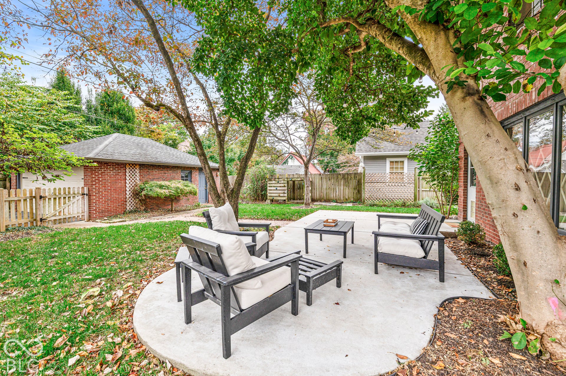 Backyard featuring a concrete patio, red brick exterior wall, detached brick garage, mature trees, and wooden perimeter fencing
