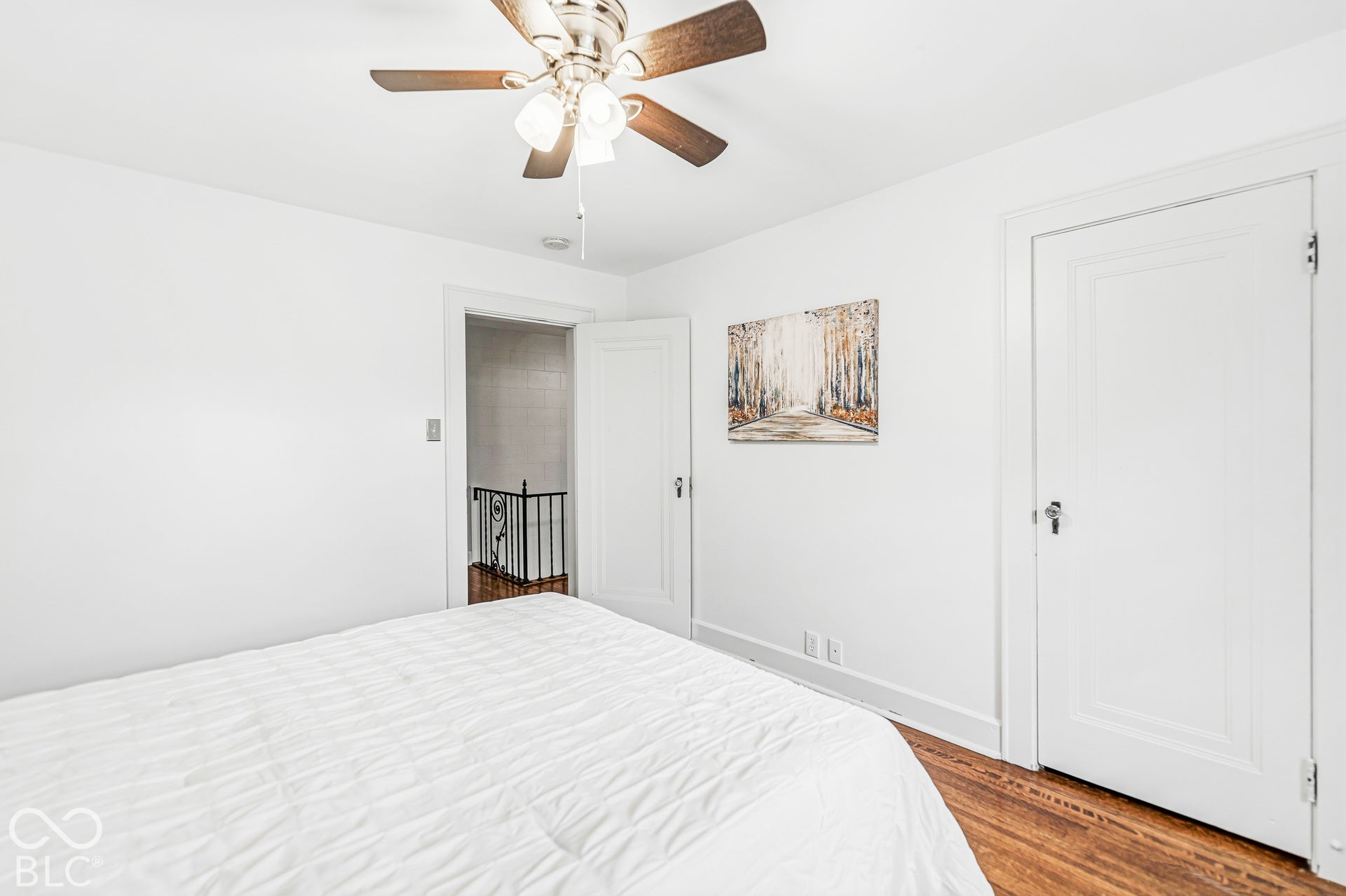 Room featuring wood-finish flooring, a multi-blade ceiling fan with integrated lighting, and solid-core interior doors with hardware