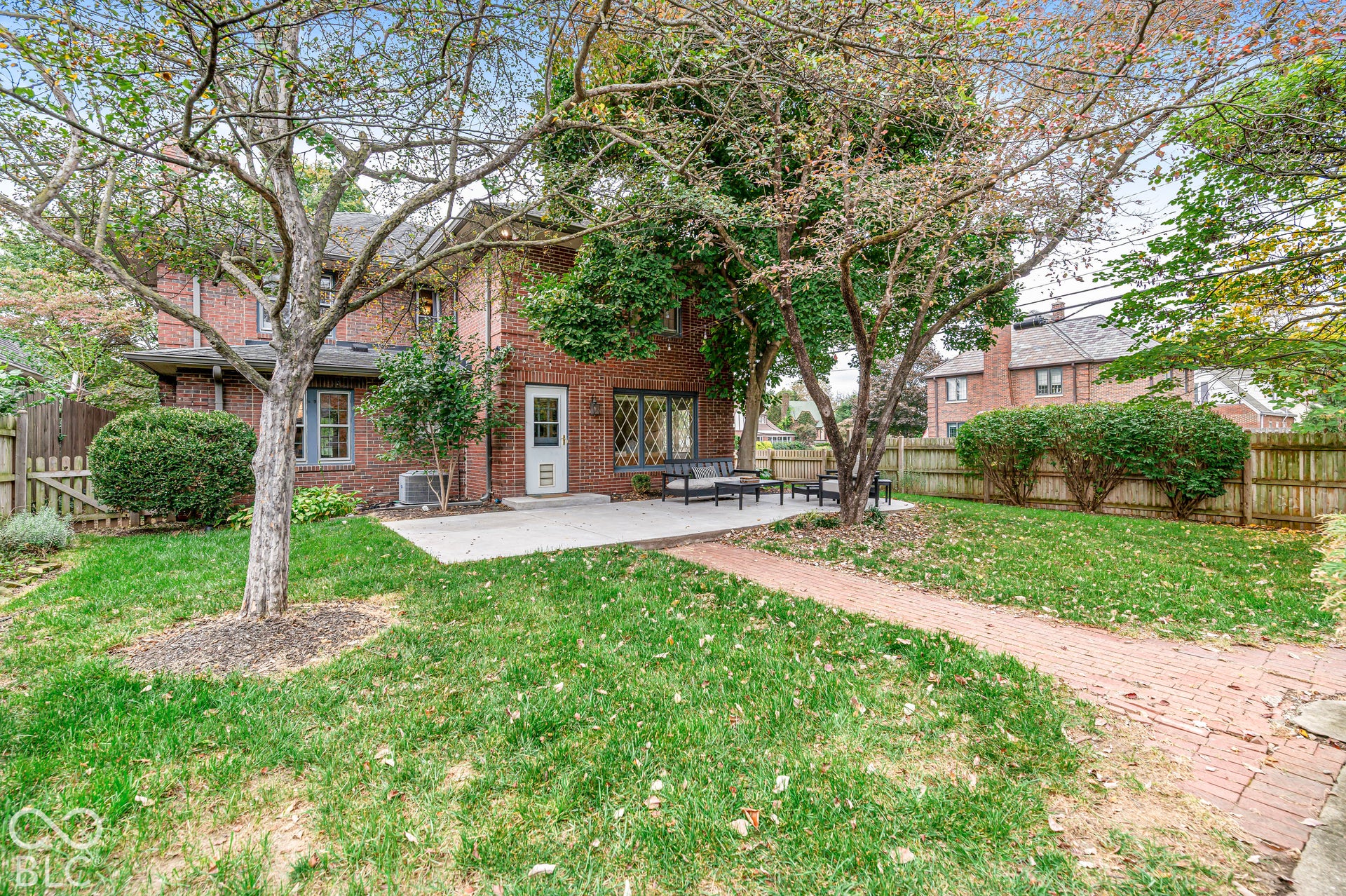 Brick exterior featuring a concrete patio, a brick paver walkway, mature trees, and wooden privacy fencing