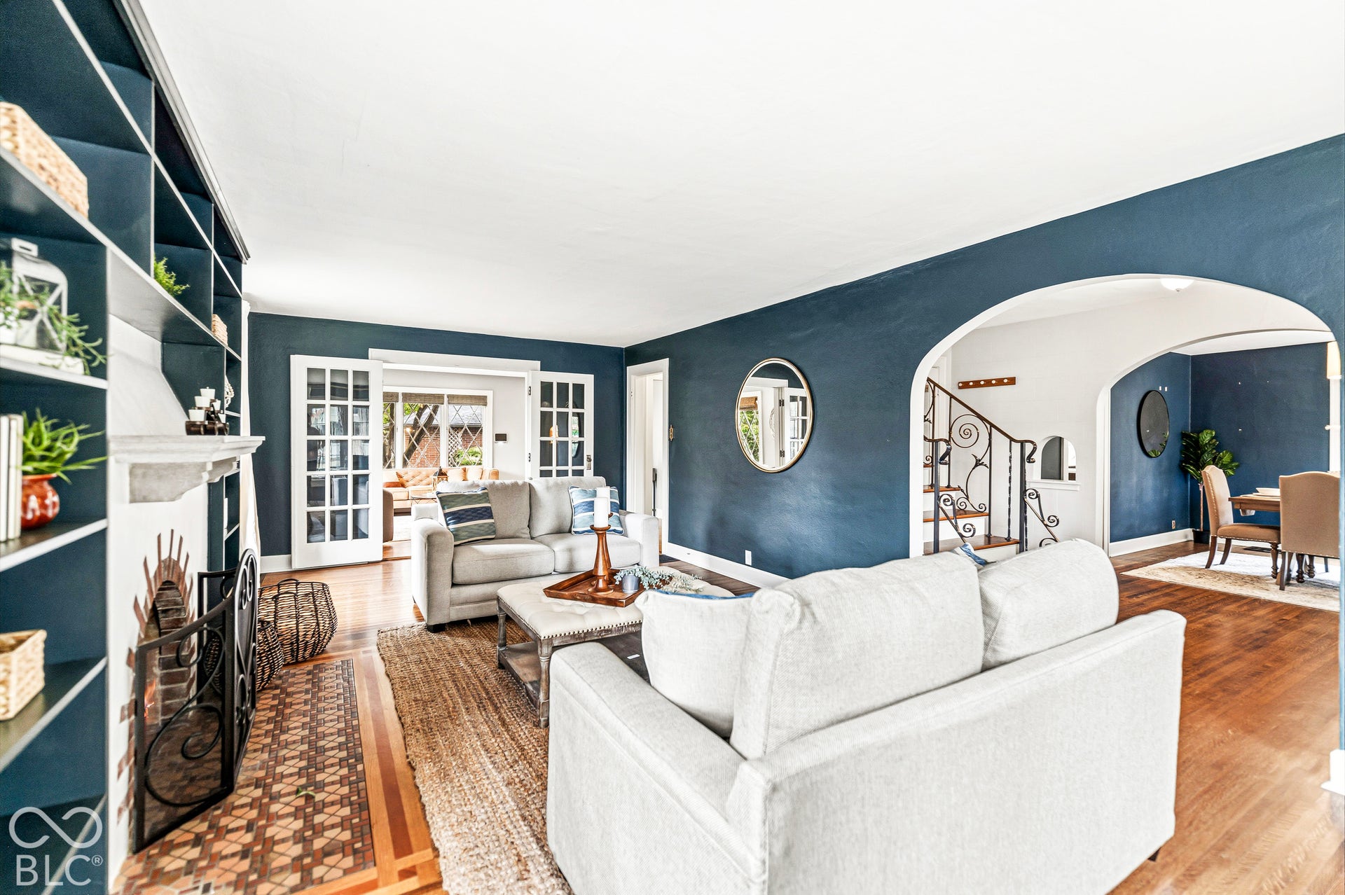 Built-in floor-to-ceiling shelving, masonry fireplace with patterned tile surround, arched entryway, and wood-finish flooring