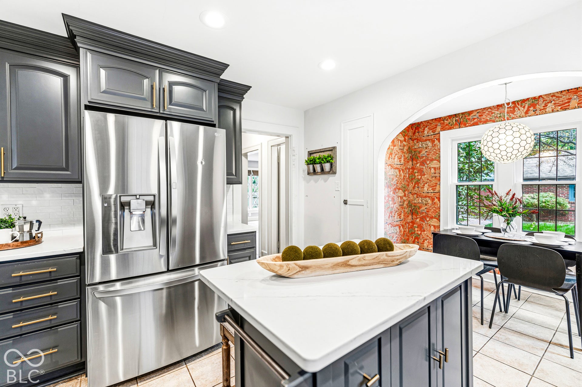 Kitchen featuring charcoal cabinetry, quartz countertops, stainless steel refrigerator, arched architectural opening, and patterned wallpaper