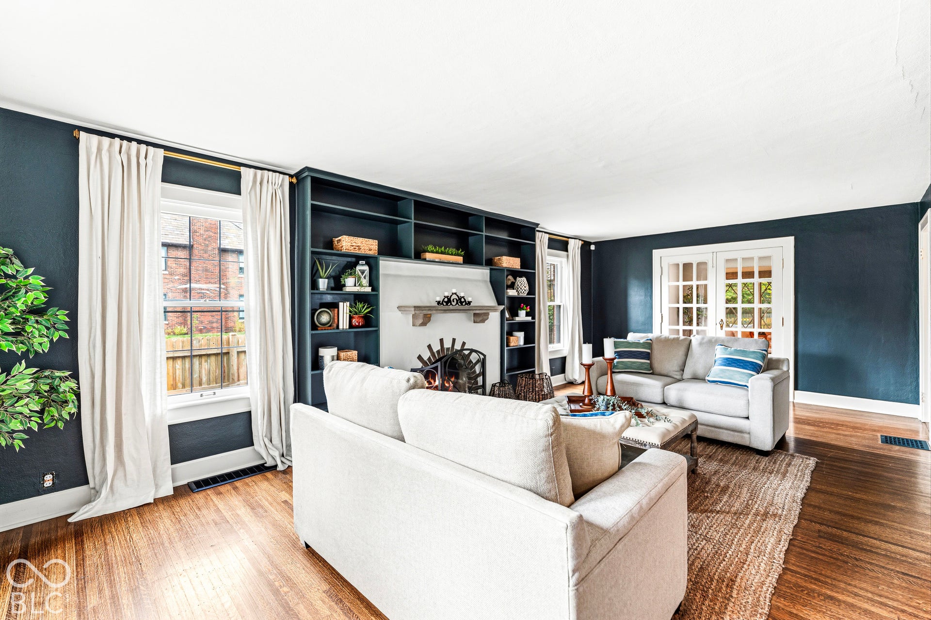 Living room featuring built-in dark cabinetry with integrated shelving, fireplace with a mantle, wood-finish flooring, and French doors