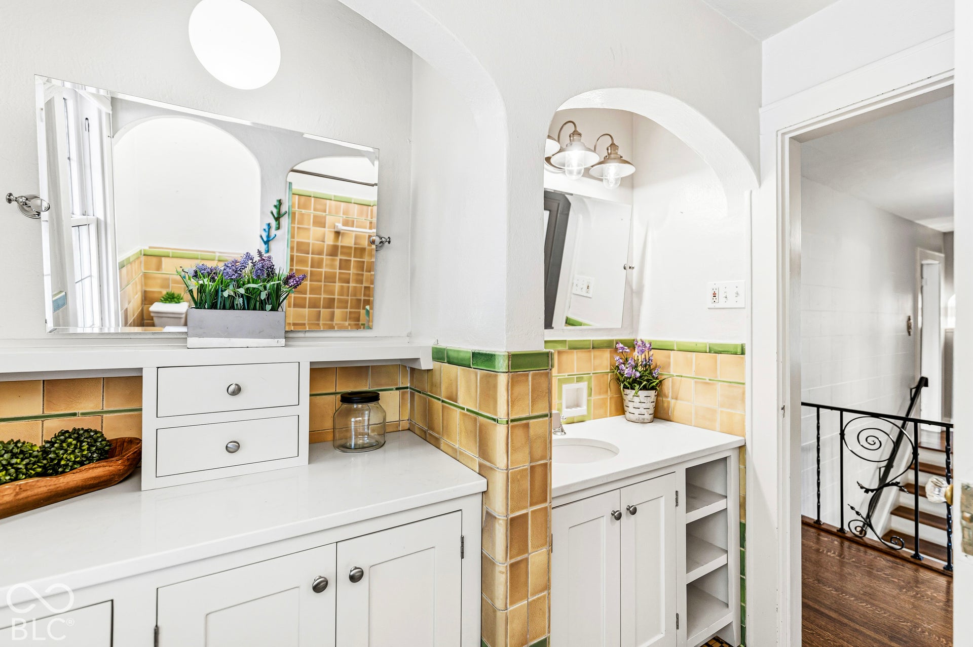 Bathroom featuring white cabinetry, light-toned countertop, arched wall alcove, and decorative tile backsplash with green accents