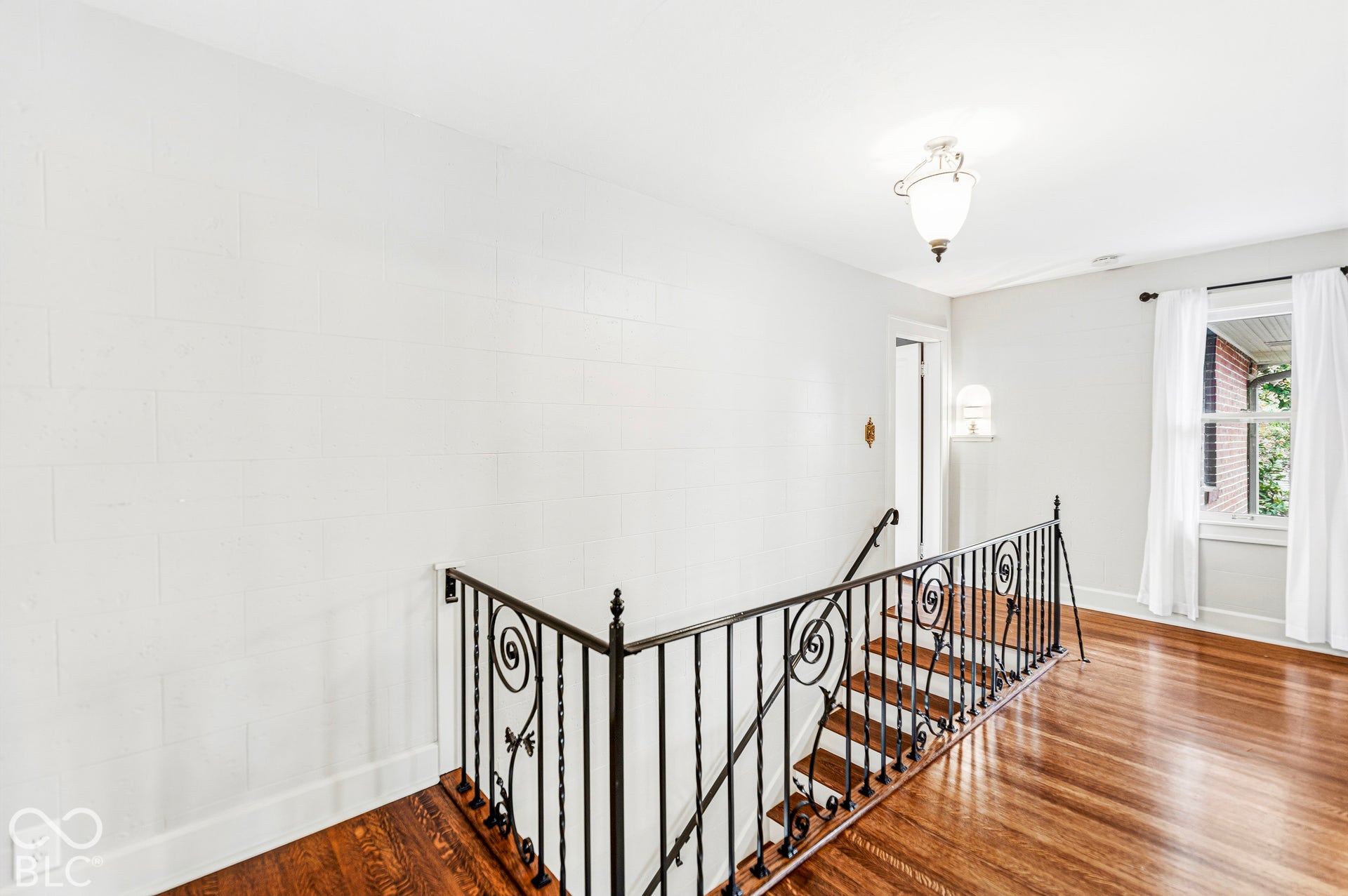 Wood-finish flooring, decorative wrought iron staircase railing, and pendant lighting