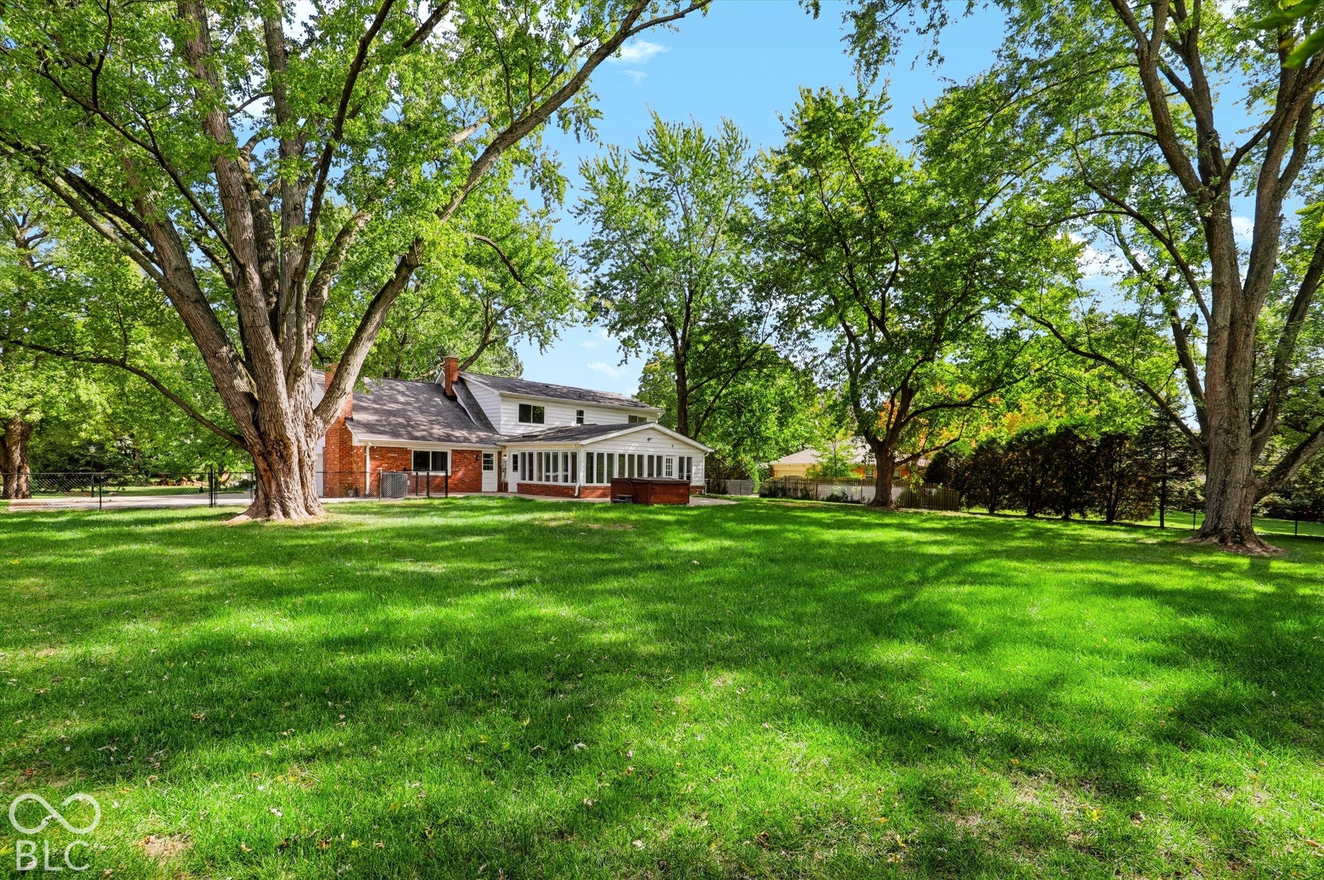 Expansive rear grounds featuring mature trees, a multi-pane sunroom, and a brick exterior