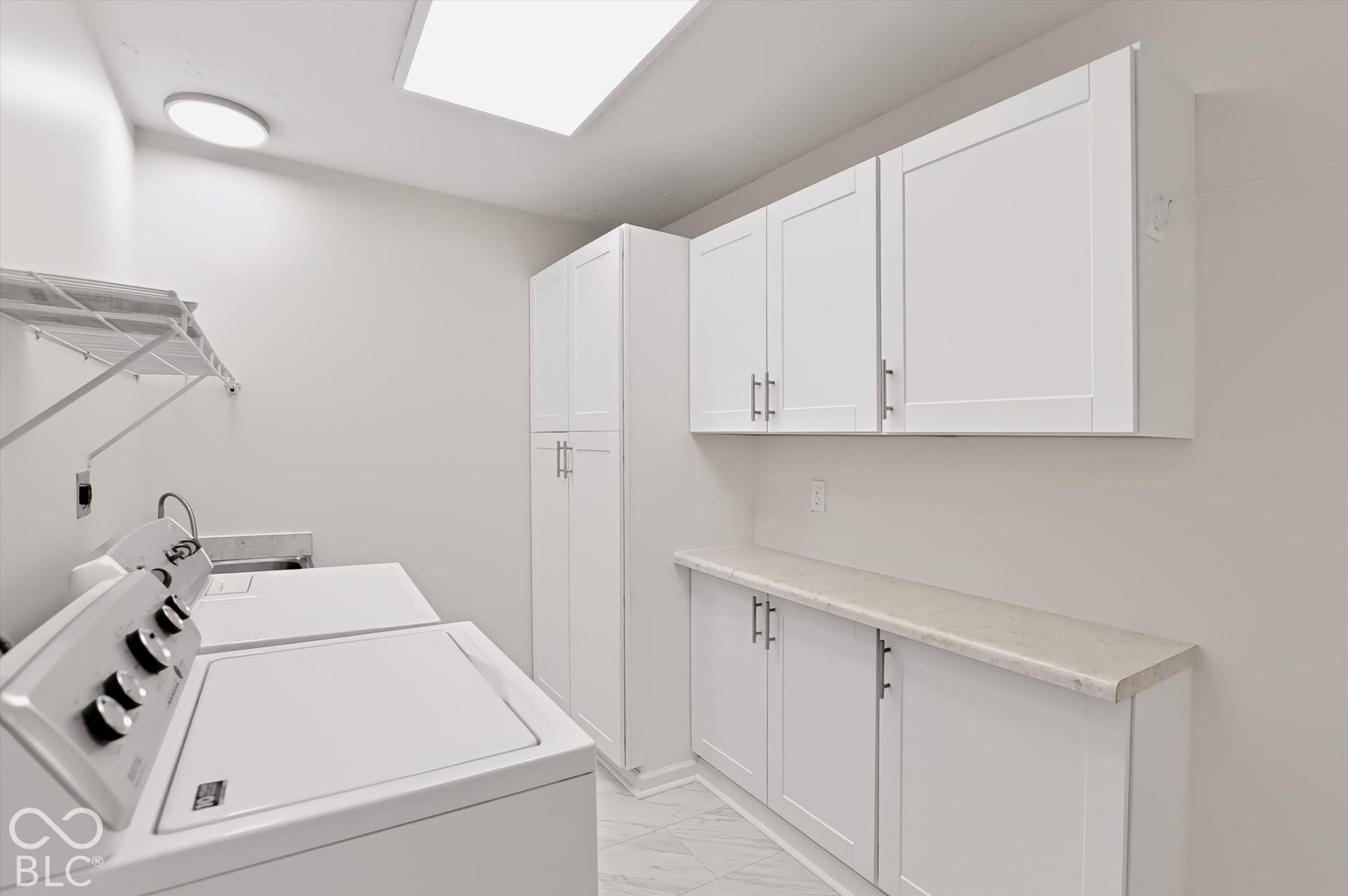 Laundry room featuring white shaker-style cabinetry, floor-to-ceiling storage, stone-finish countertops, and large-format tile flooring