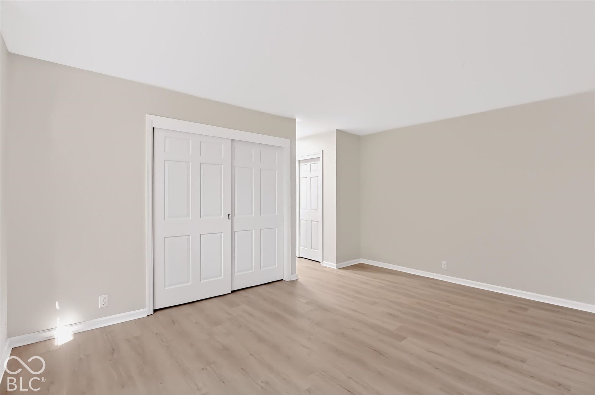 Neutral-toned interior space featuring wood-finish flooring, white six-panel sliding closet doors, and white paneled swinging doors