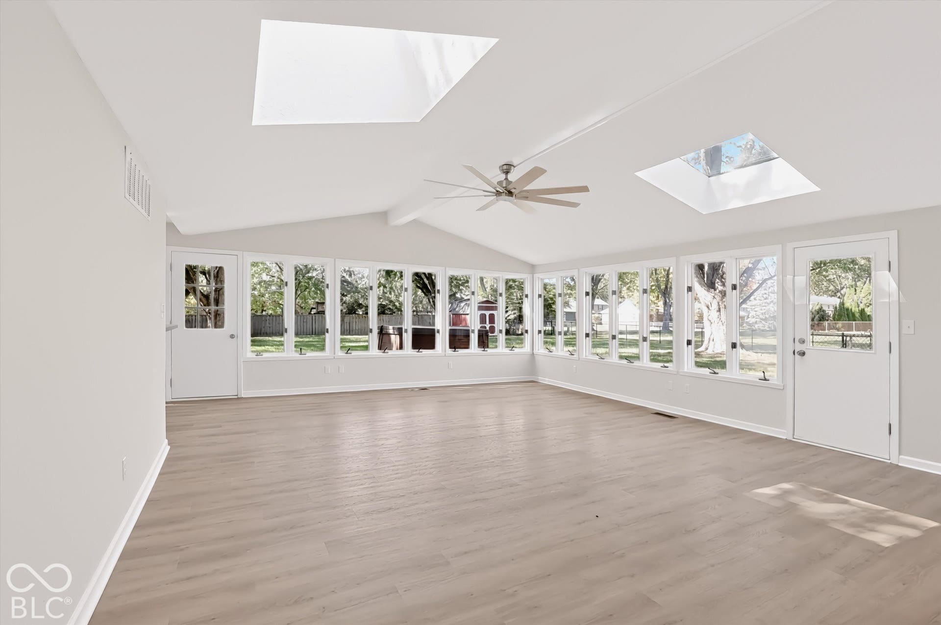 Sun-filled interior featuring vaulted ceilings, multiple skylights, extensive window walls, wood-finish flooring, and a ceiling fan