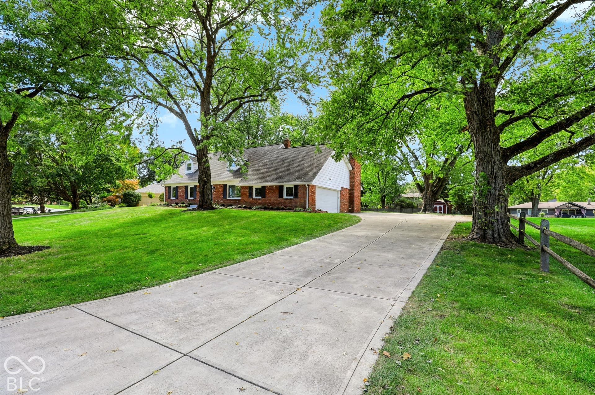 Brick and siding exterior featuring a concrete driveway, mature canopy trees, and expansive lawn