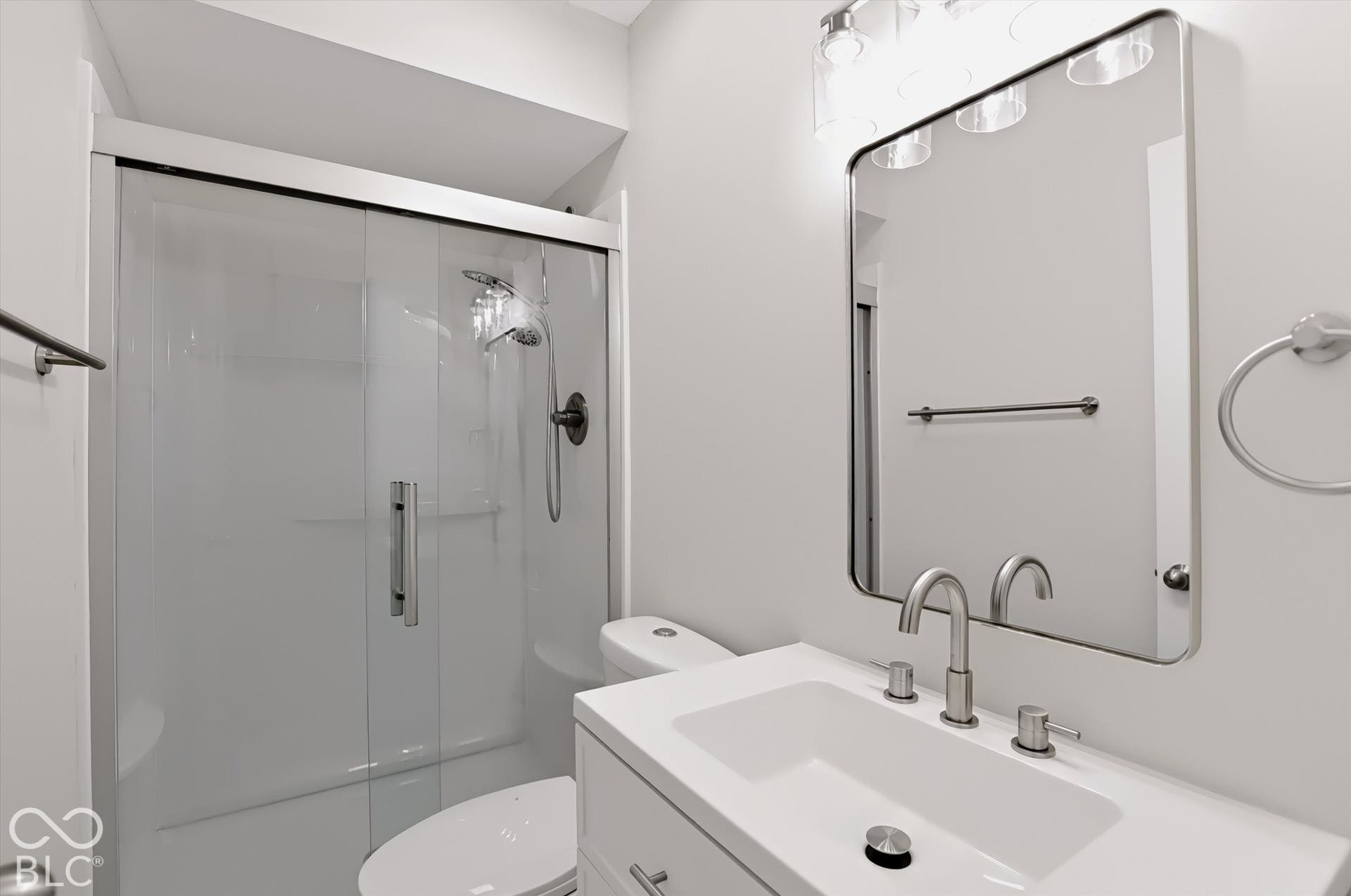 Bathroom featuring a vanity with an integrated rectangular sink, a frameless sliding glass shower door, a brushed nickel widespread faucet, and a rectangular mirror with rounded corners