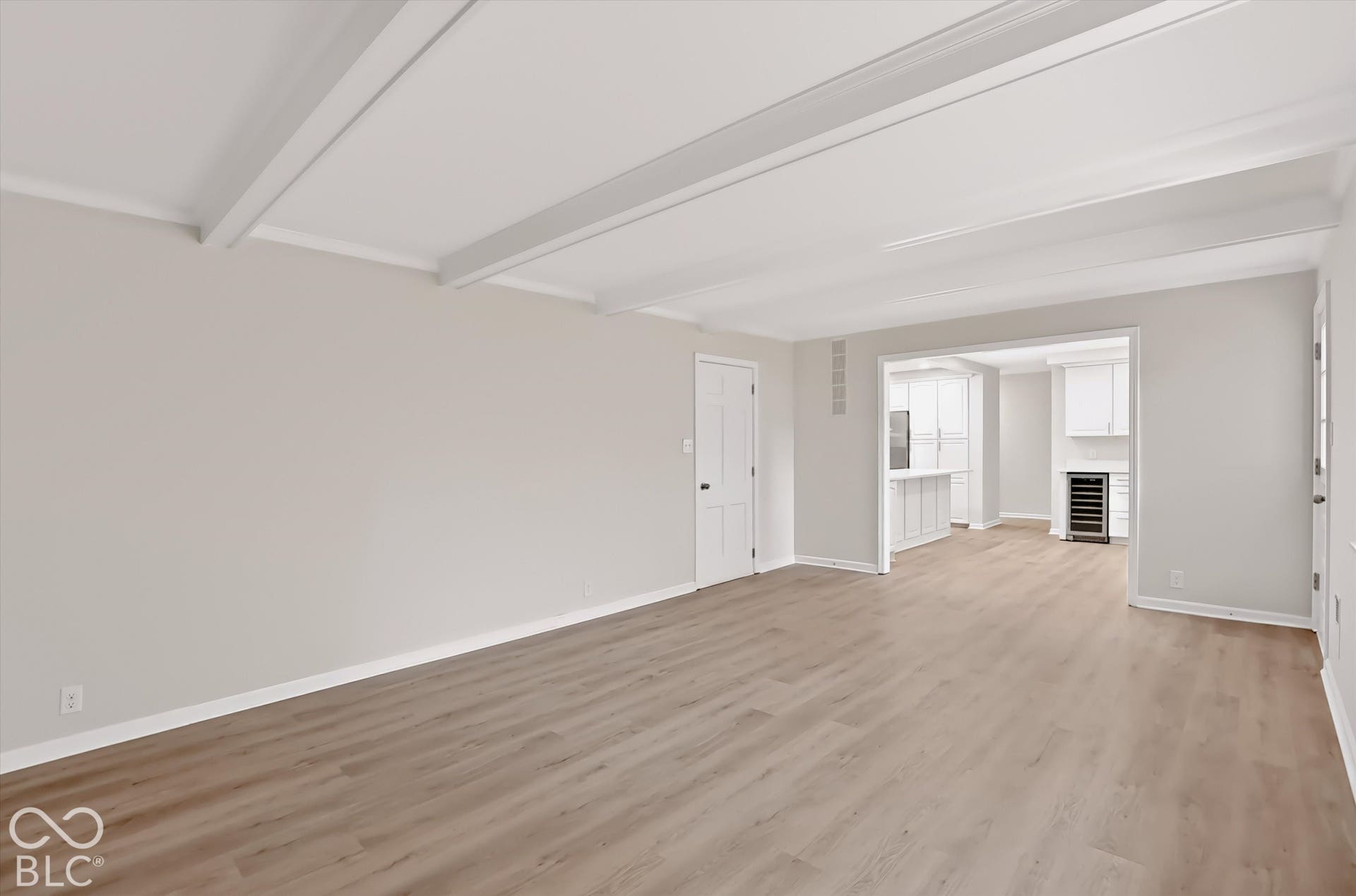 Open-concept interior featuring wood-finish flooring, exposed ceiling beams, and a built-in wine refrigerator