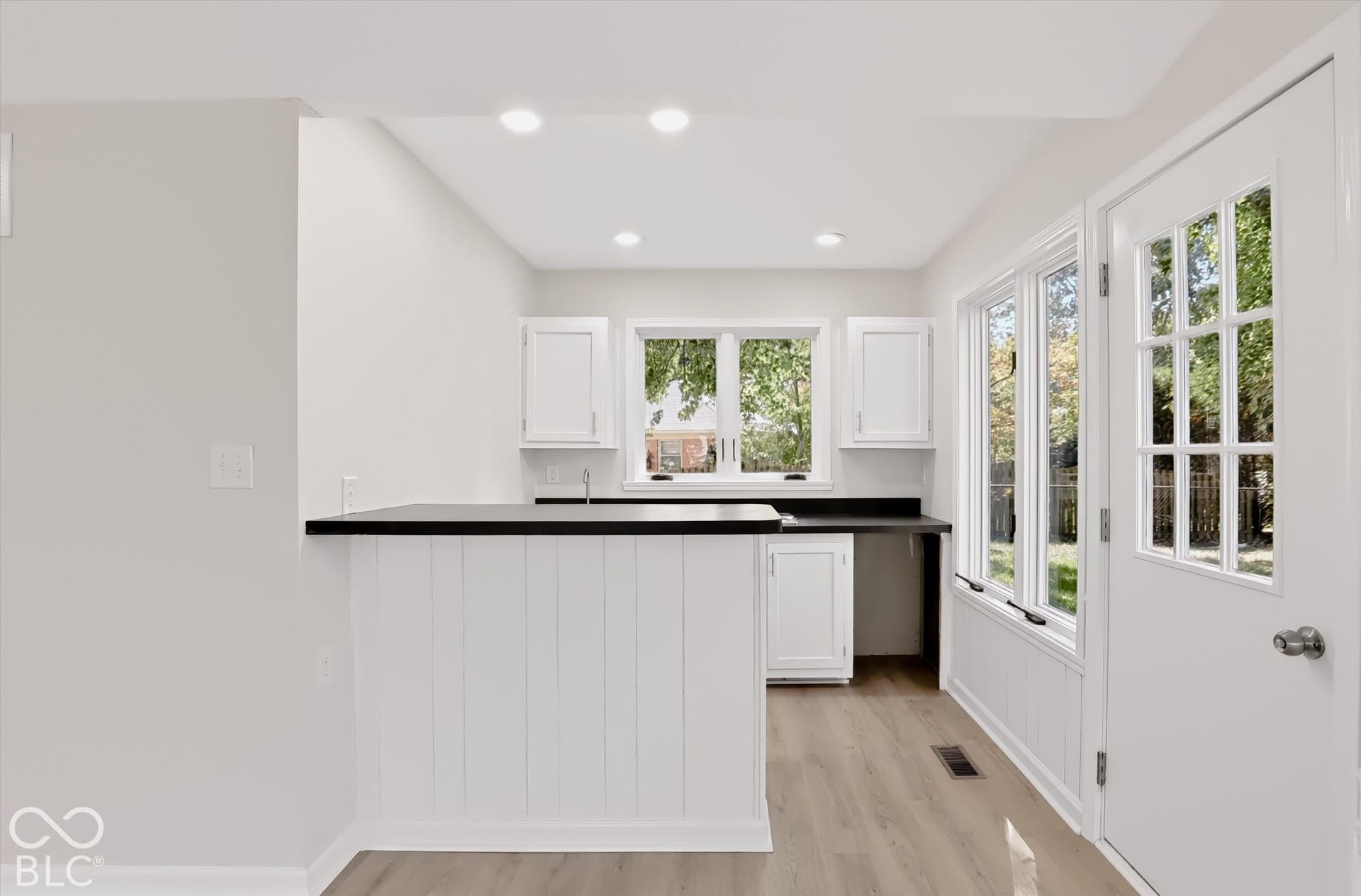 Kitchen featuring white shaker-style cabinetry, dark contrast countertops, wood-finish flooring, recessed lighting, and a multi-pane glass entry door