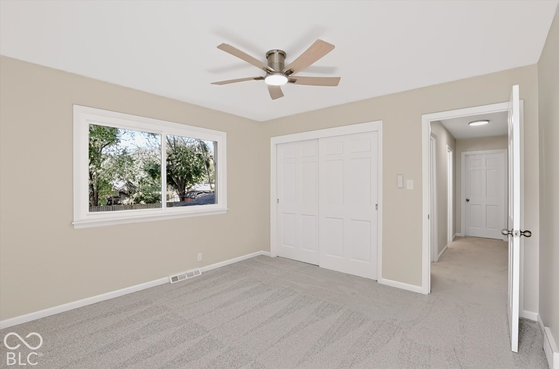 Neutral wall finishes with neutral carpeting, built-in dual-panel sliding closet doors, and a ceiling fan with integrated lighting