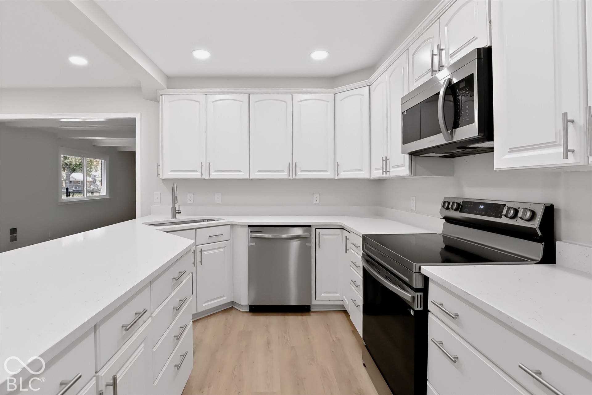 Kitchen featuring white cabinetry with brushed nickel hardware, solid surface countertops, recessed lighting, and stainless steel appliances including a range, microwave, and dishwasher, complemented by wood-finish flooring
