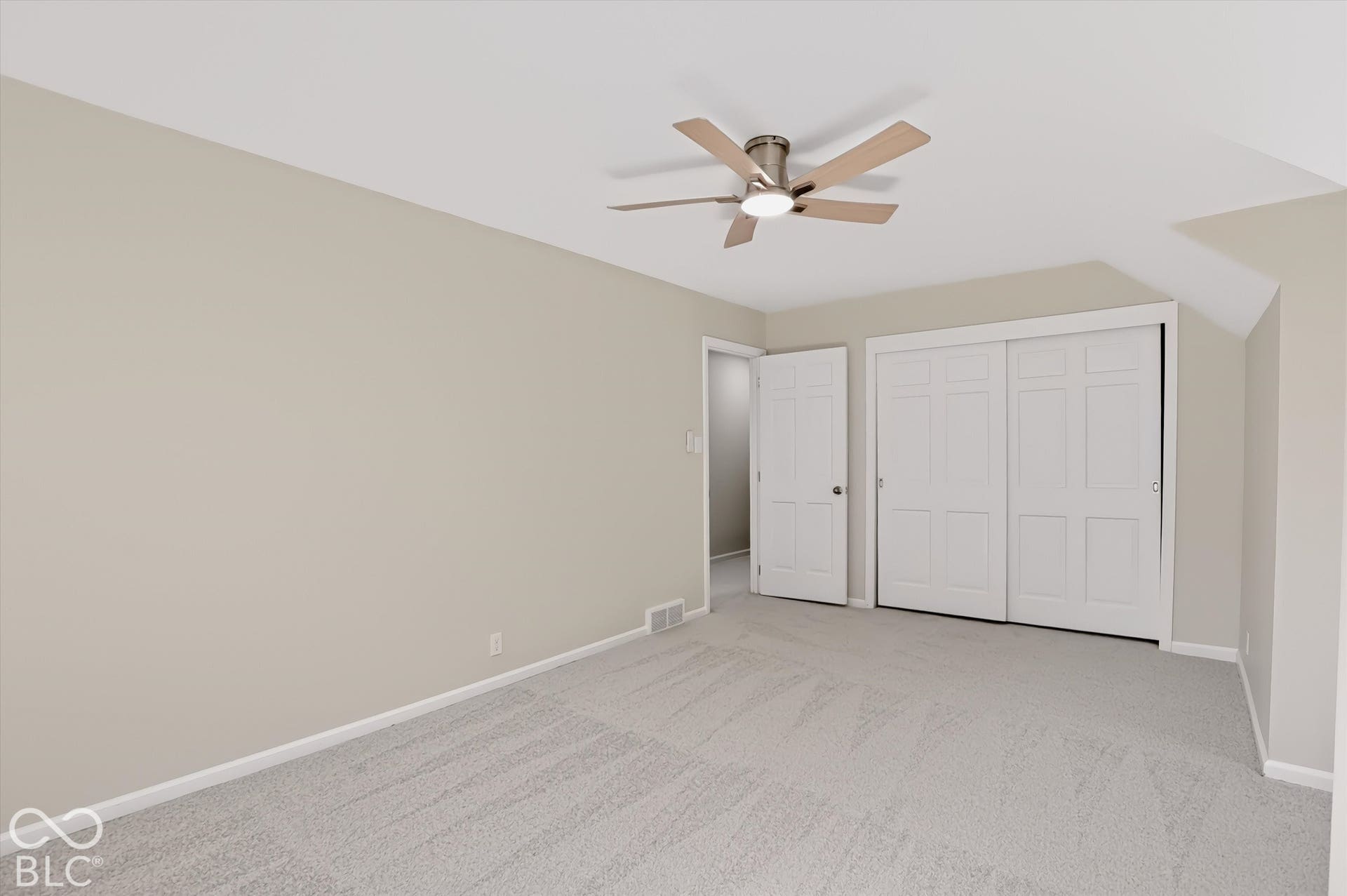 Neutral-toned room featuring wall-to-wall carpeting, a ceiling fan with integrated lighting, and a double-panel sliding closet