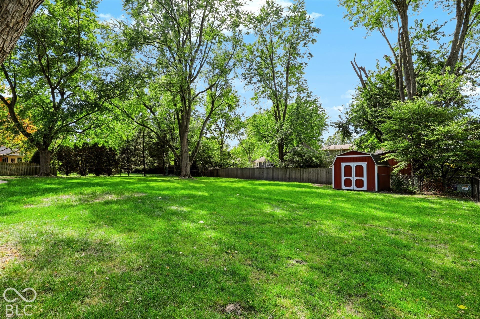 Expansive backyard featuring a grass lawn, mature trees, wood privacy fencing, and an exterior storage shed
